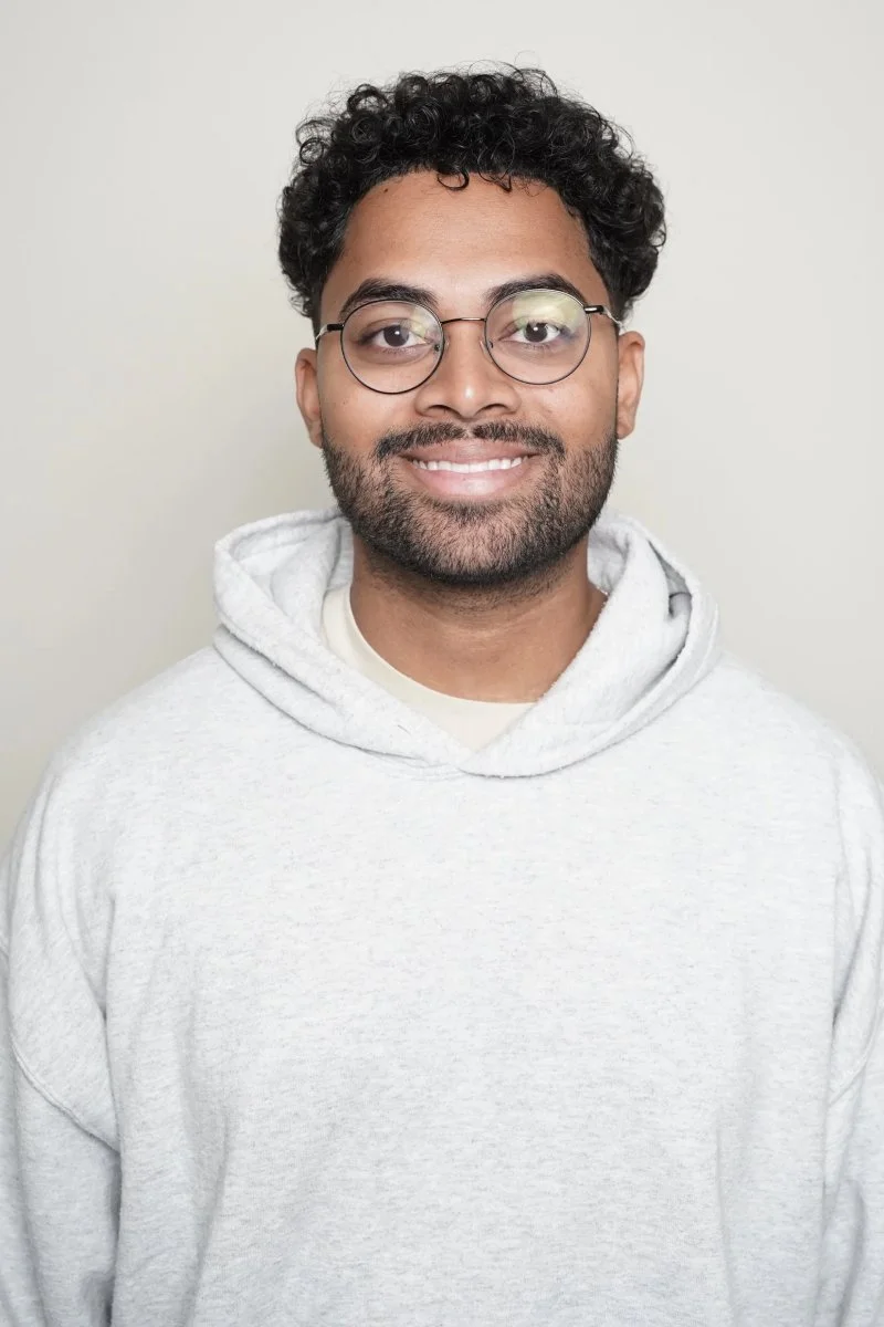Portrait d'un homme souriant avec des lunettes, portant un hoodie gris clair, fond neutre.