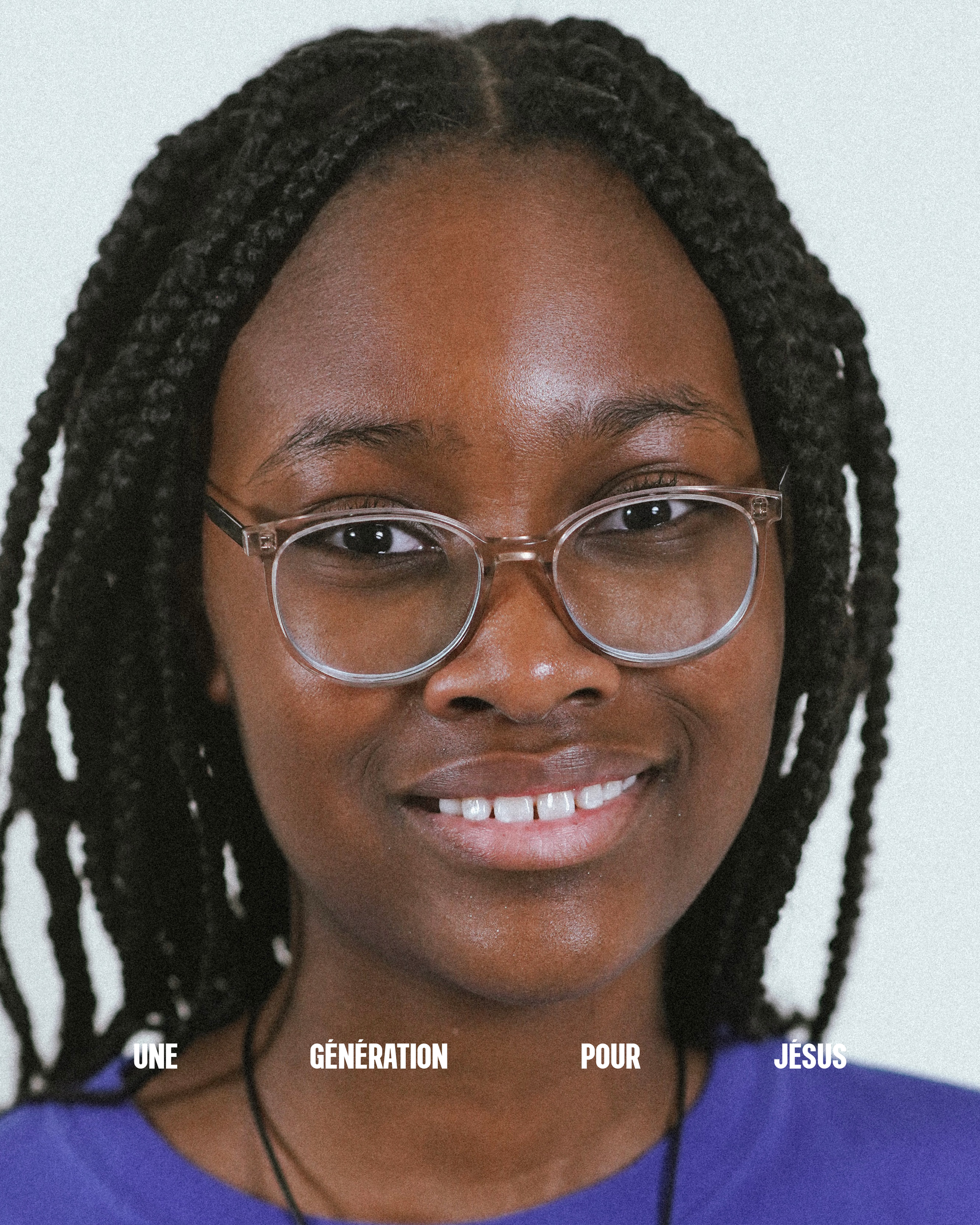 Un portrait d'une femme souriante portant des lunettes, avec des cheveux en tresses, portant un vêtement bleu clair.