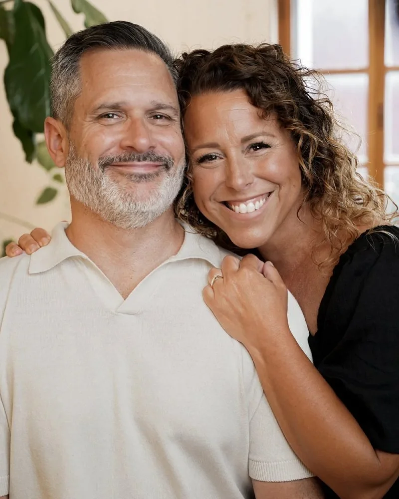 Un homme et une femme souriants en proximité, dans une pièce éclairée avec une fenêtre en arrière-plan.