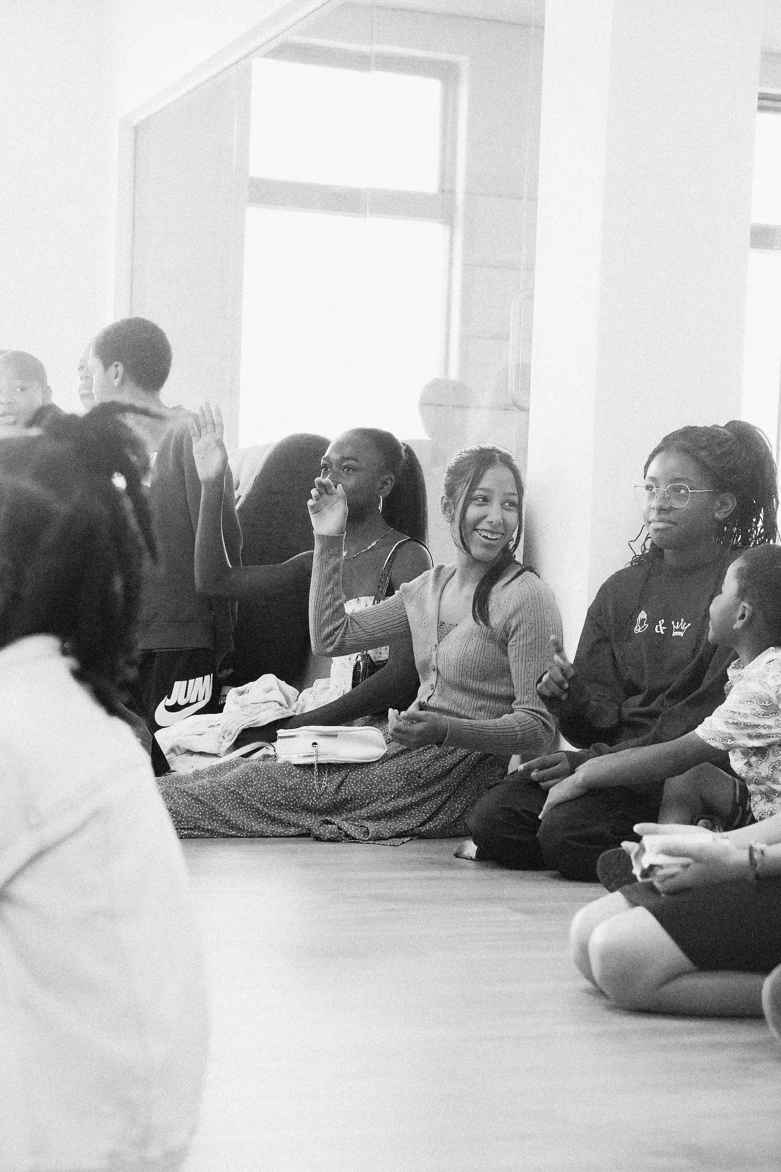 Groupe de personnes assises par terre lors d'une discussion ou d'un atelier, dont deux femmes souriantes en détail.