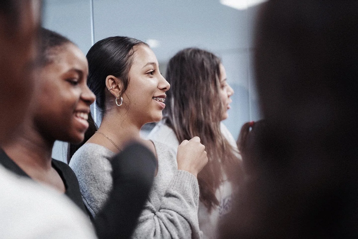 Quatre jeunes femmes assises côte à côte, souriantes et engagées, dans une salle, probablement lors d'une réunion ou d'un atelier, l'ambiance semble amicale et positive.