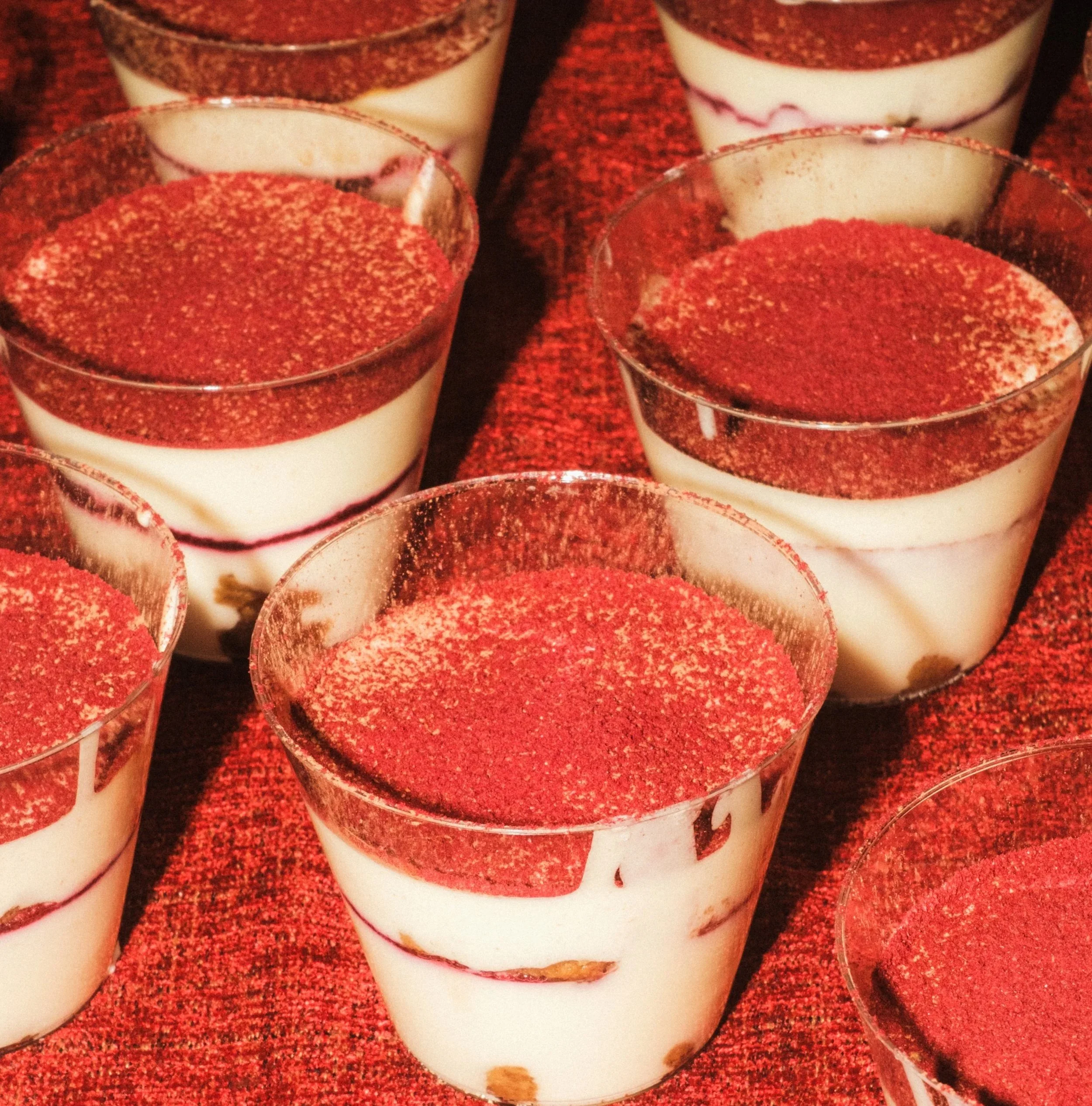 Multiple individual servings of layered tiramisu in clear cups, topped with raspberry powder.