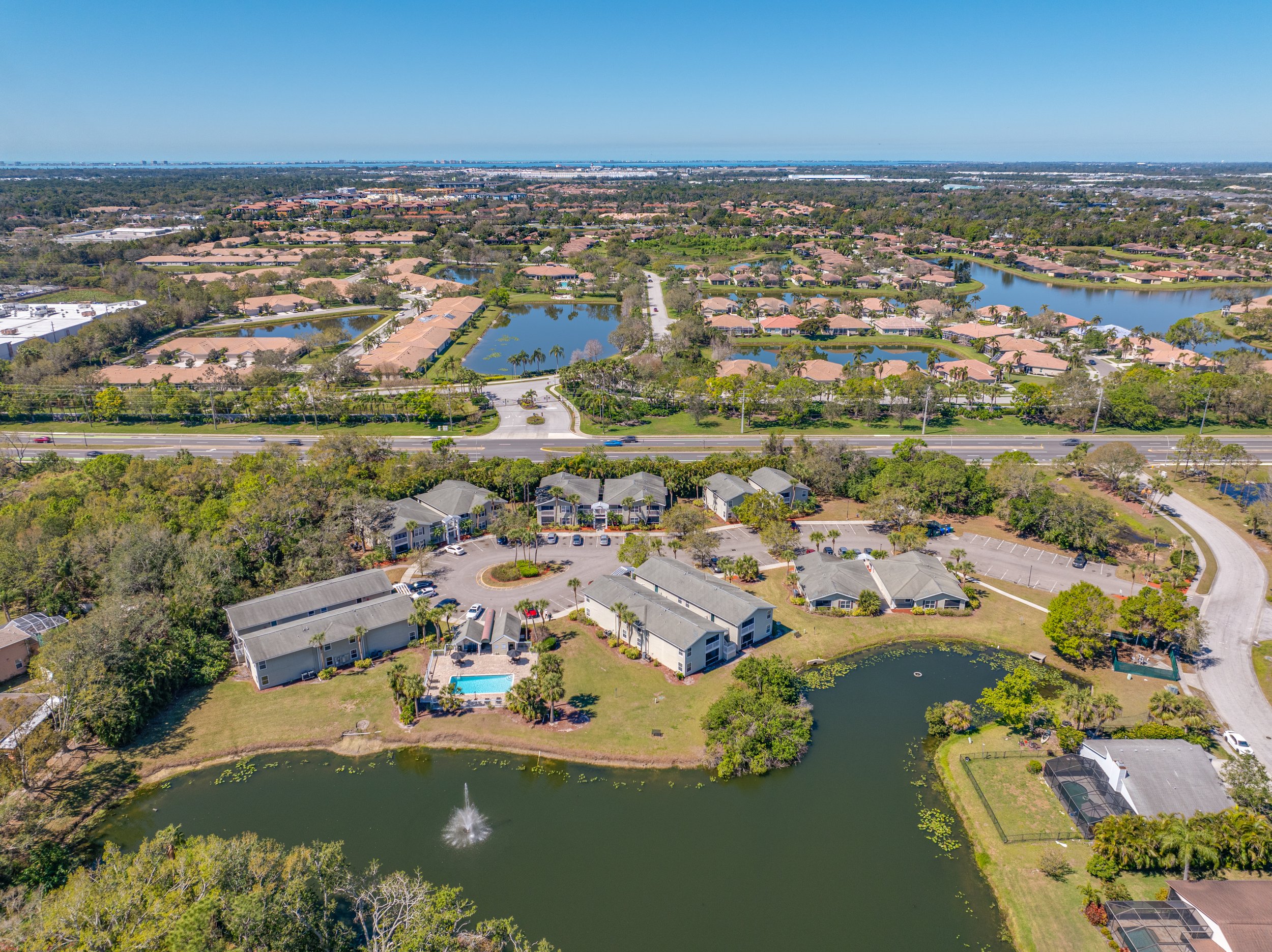 Aerial view of a suburban neighborhood with lakes, roads, and green spaces, including residential houses, parking lots, and a small pond with a fountain.