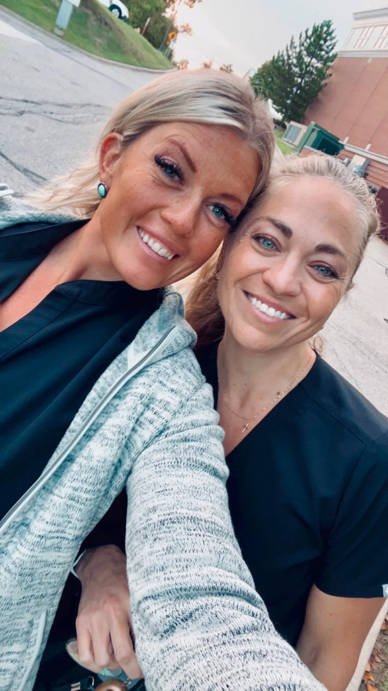 Two women taking a selfie outdoors during sunset, smiling and close together.