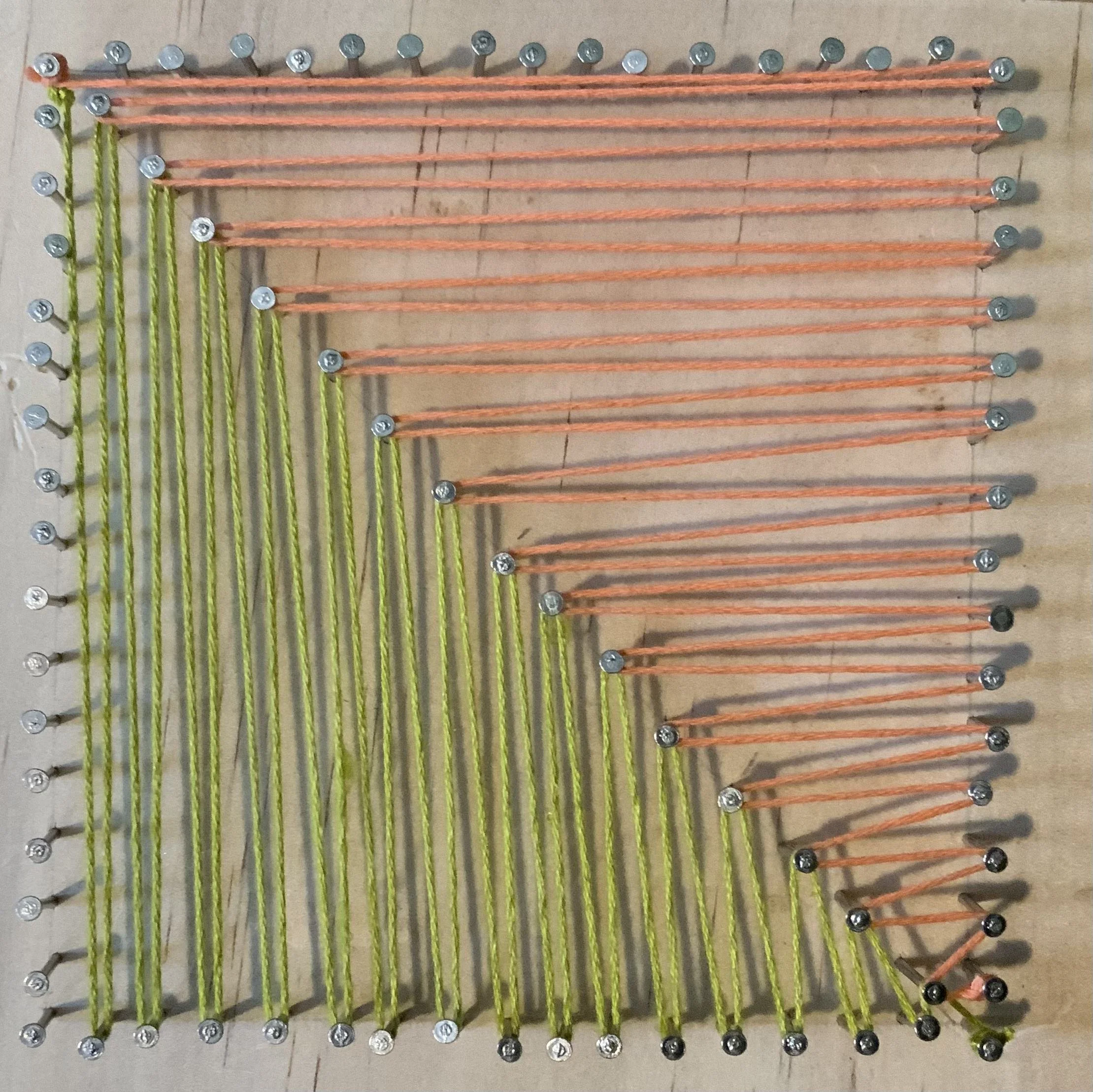 A wooden board with nails arranged in a grid and colored strings looped around the nails to create a pattern. (Created by O.E. Zelmanovich. Zoe Zelmanovich. Zoe Mizuho)