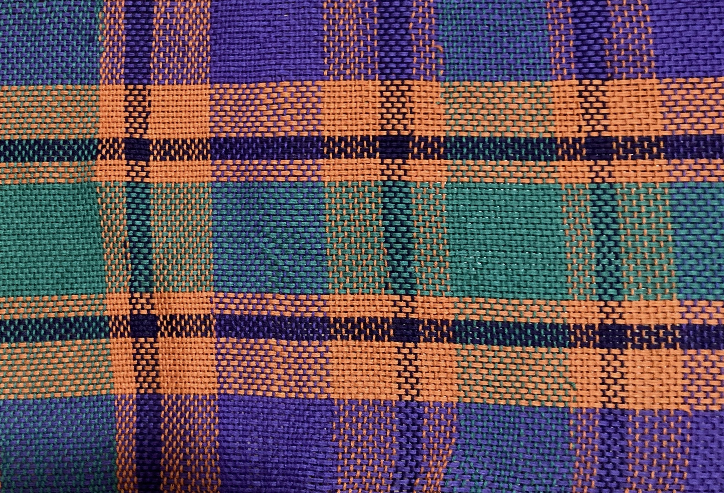Close-up of a multicolored woven fabric with a plaid pattern incorporating orange, purple, green, and teal colors. (Created by O.E. Zelmanovich. Zoe Zelmanovich. Zoe Mizuho)