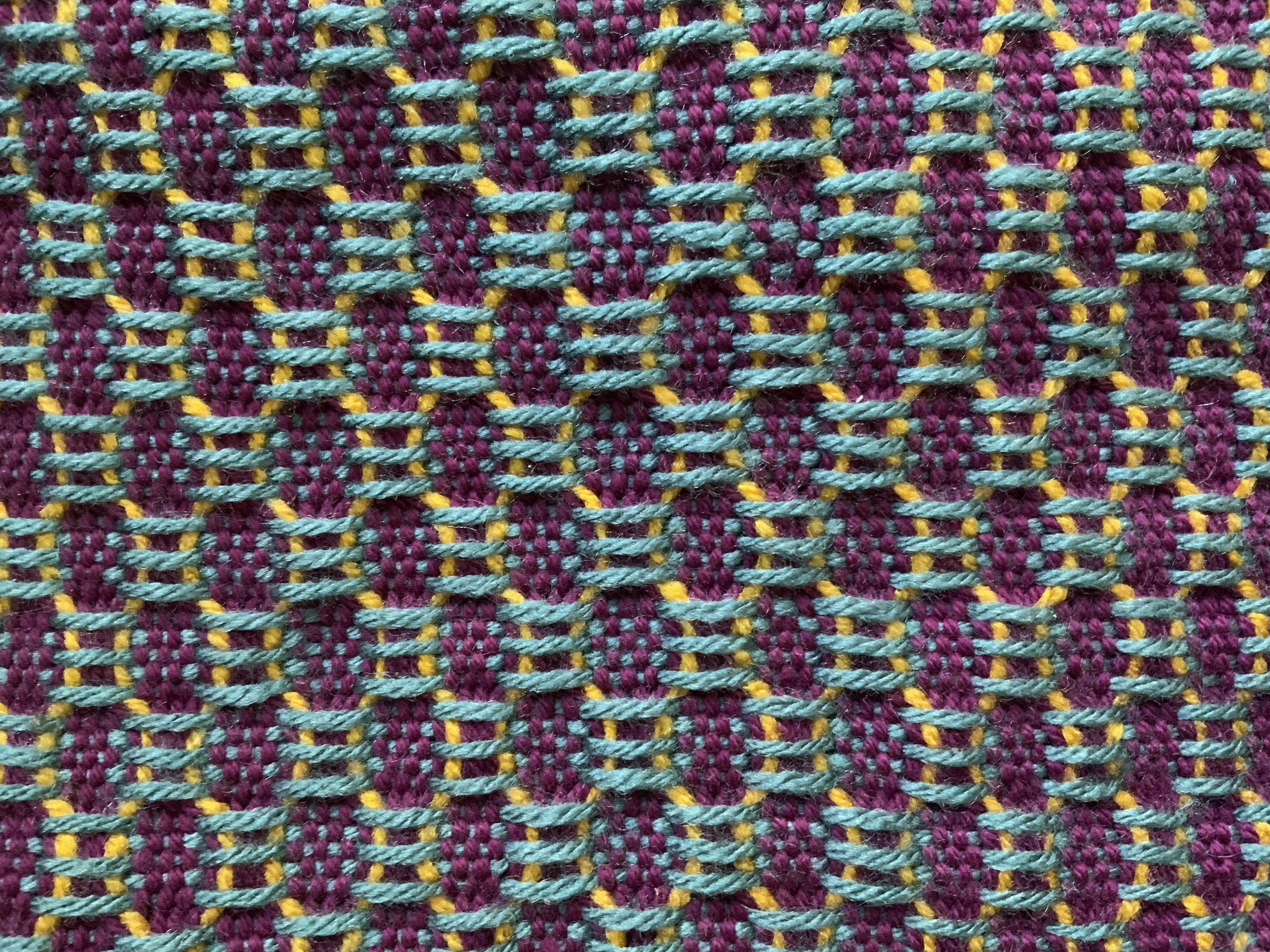 Close-up of a colorful woven textile with pink, turquoise, yellow, and purple threads creating a geometric pattern. (Created by O.E. Zelmanovich. Zoe Zelmanovich. Zoe Mizuho)