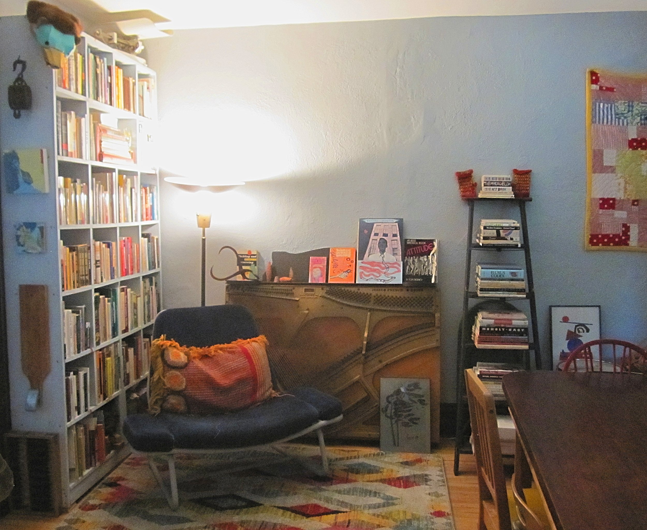 Stylish living room with a tall bookshelf filled with books, a lamp, and artwork. (Designed by O.E. Zelmanovich. Zoe Zelmanovich. Zoe Mizuho)
