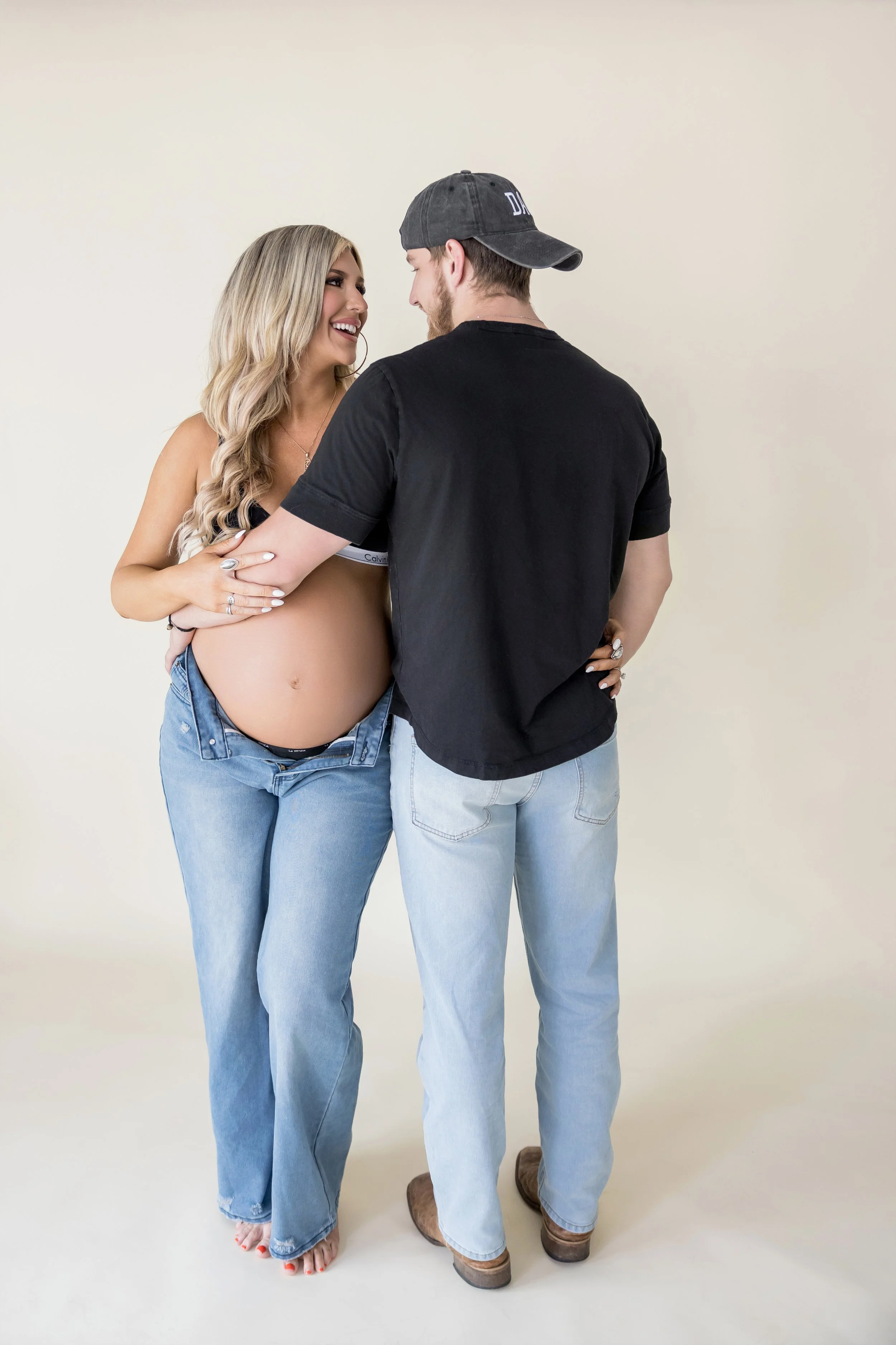 Natural light studio maternity portrait featuring an expectant mother in a modern white outfit.