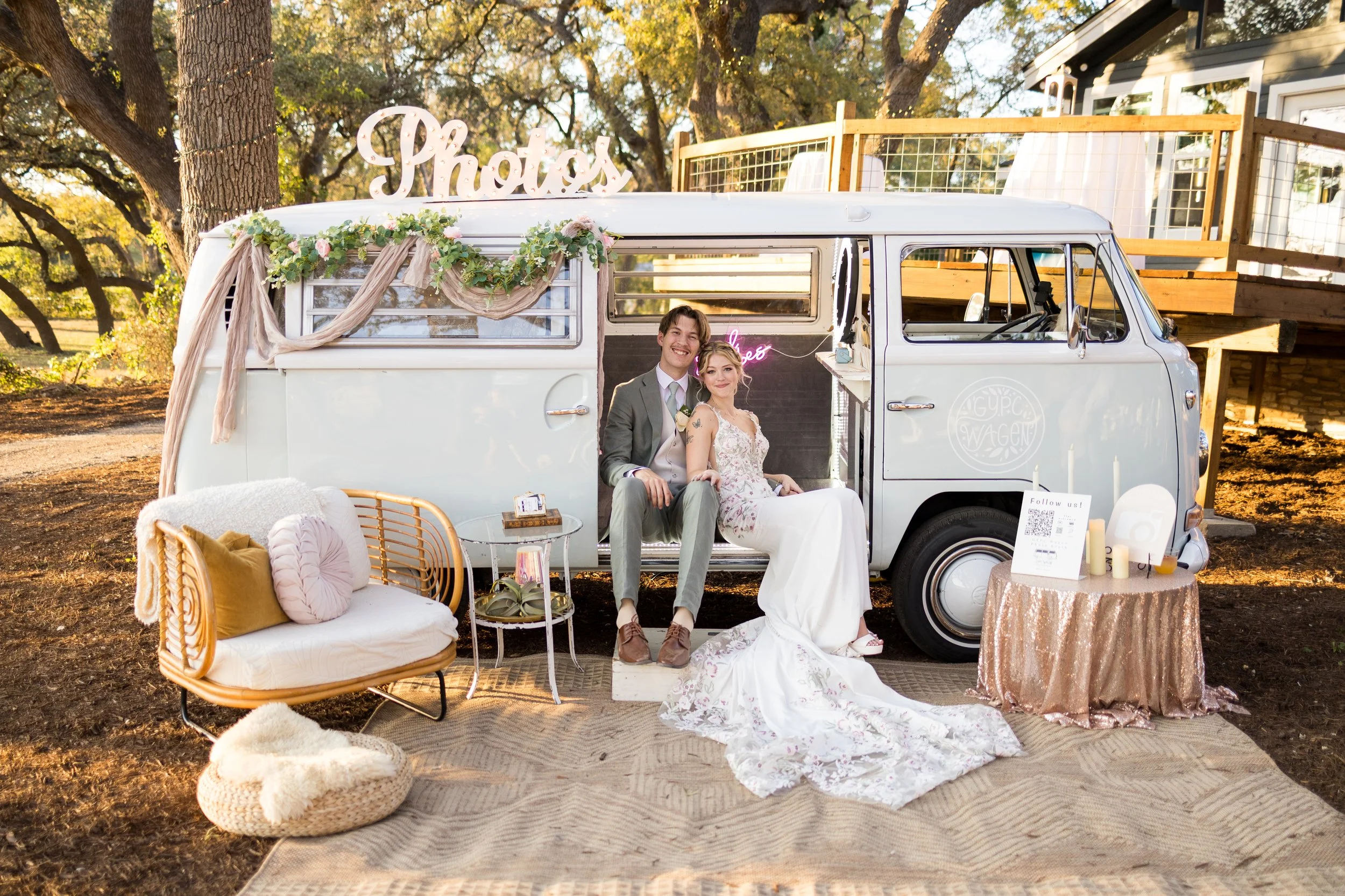 Bride and groom seated in a vintage Volkswagen photo booth bus during an elegant outdoor wedding celebration