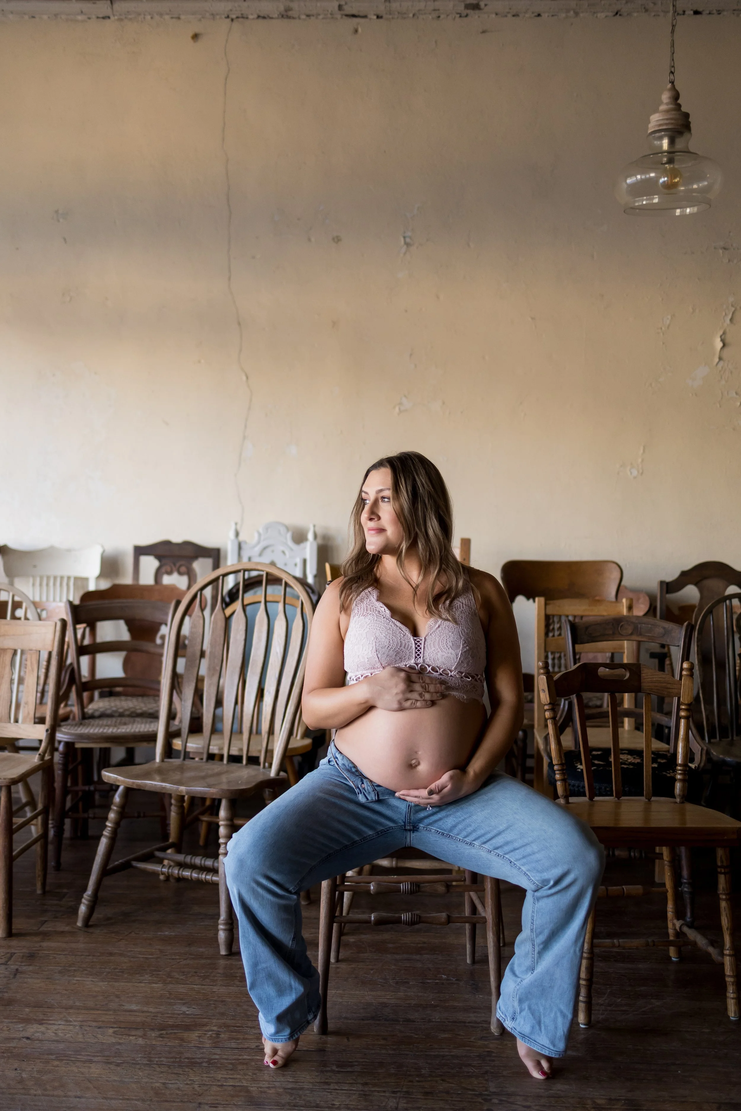 An intimate indoor maternity portrait captured in natural window light, featuring an expectant mother reclining on a vintage sofa in a casual clothing.