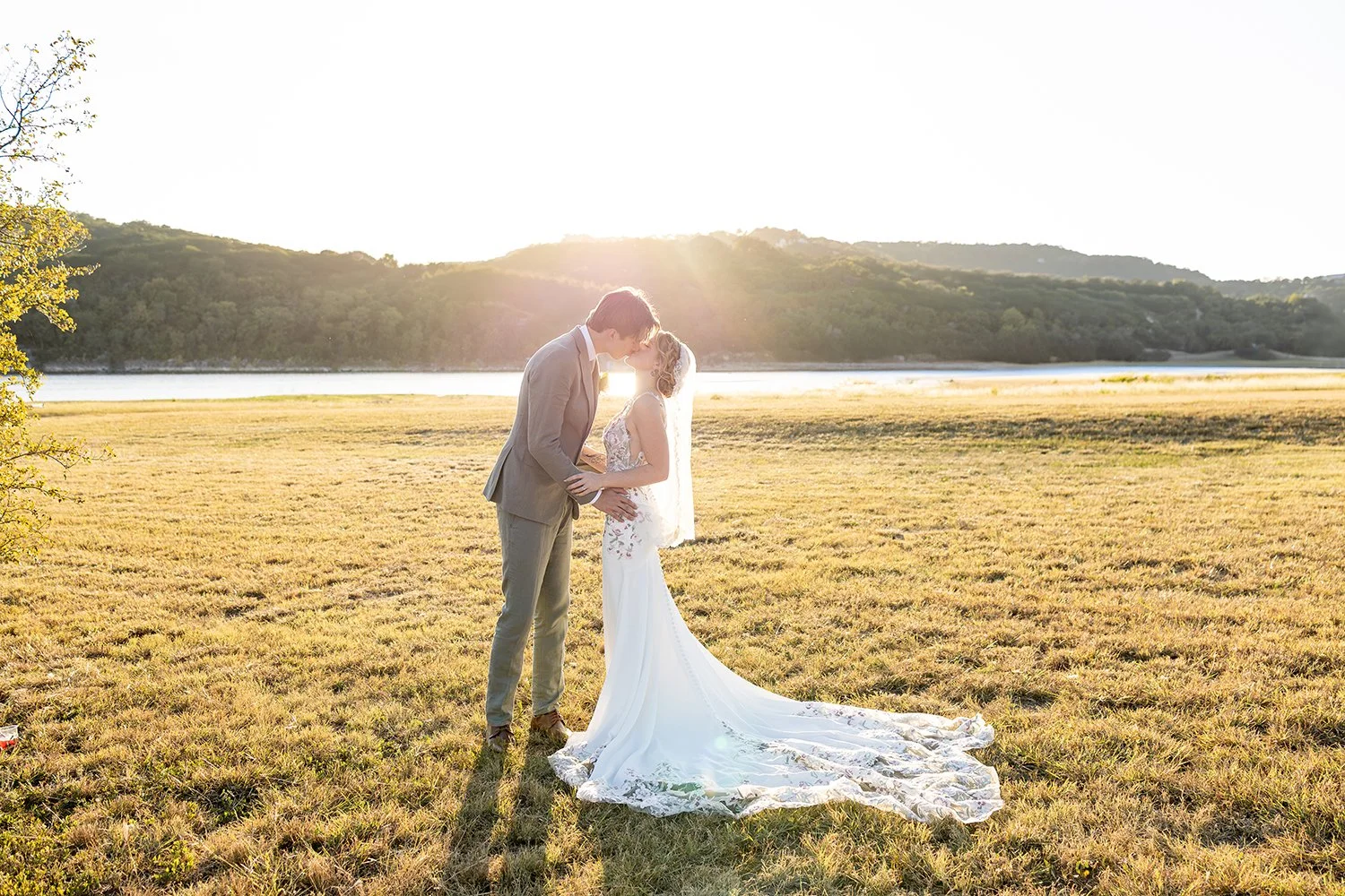 Bride and groom sharing a sunset kiss in an open field during an elegant outdoor wedding