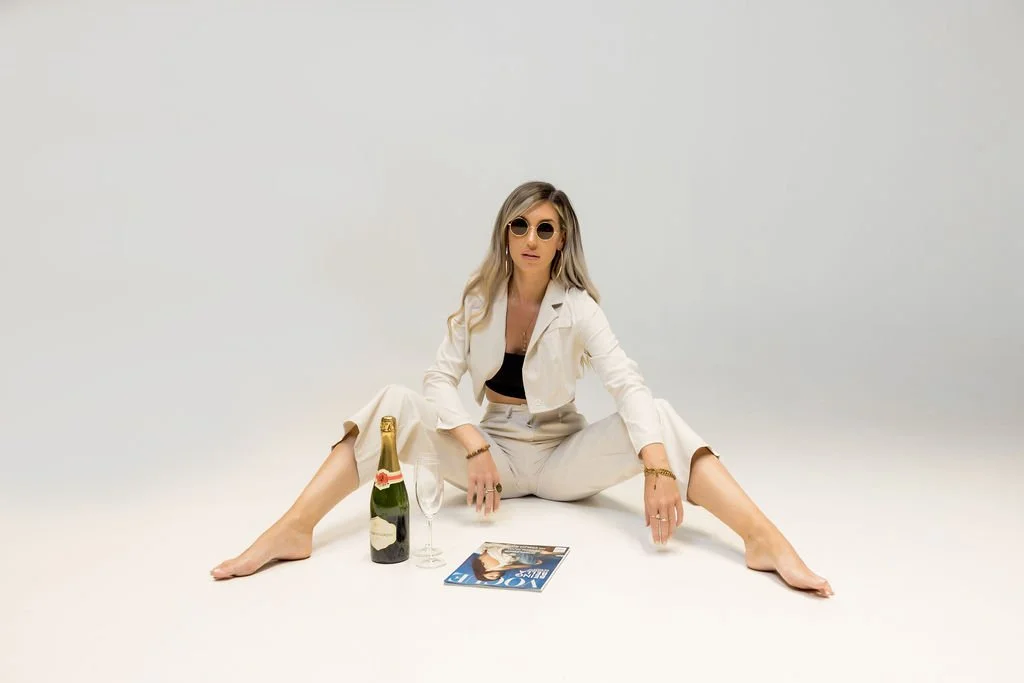 Editorial studio portrait featuring a confident woman styled in a modern neutral suit with fashion-inspired props.