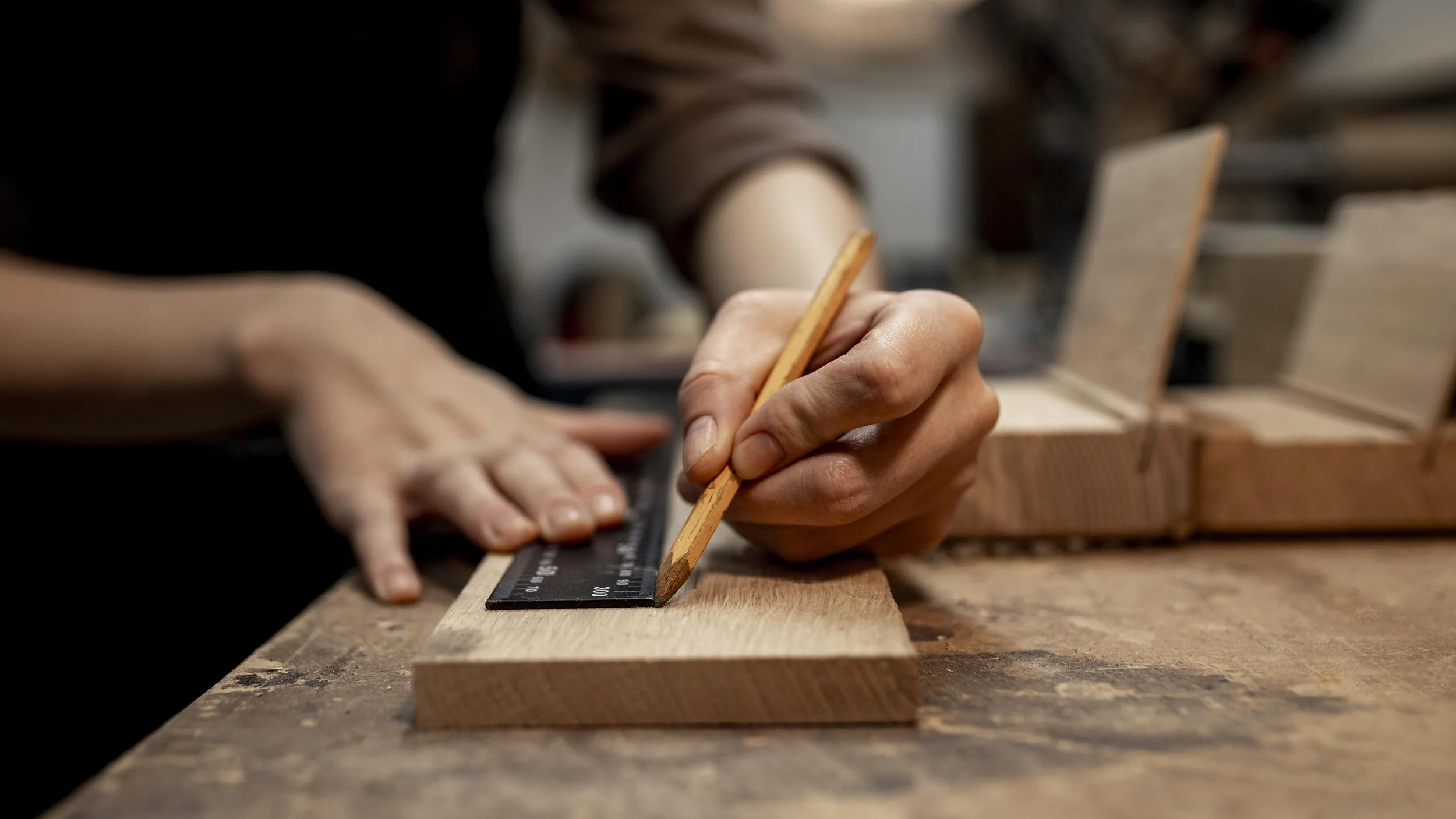 A close up of hands holding a piece of wood and making a mark with a pencil and a ruler.