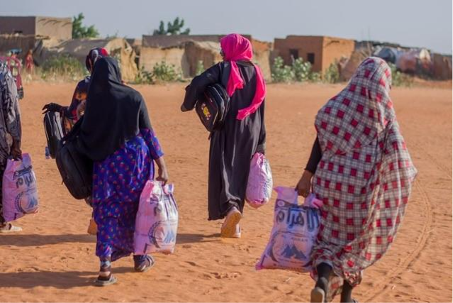 Sudanese women disperse from a HAS aid point carrying sacks of food and other items.