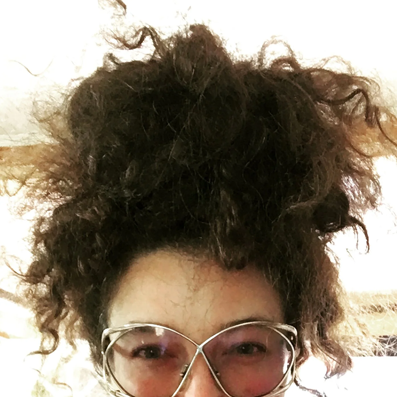 Close-up of a person's face and hair, showing glasses and curly hair.