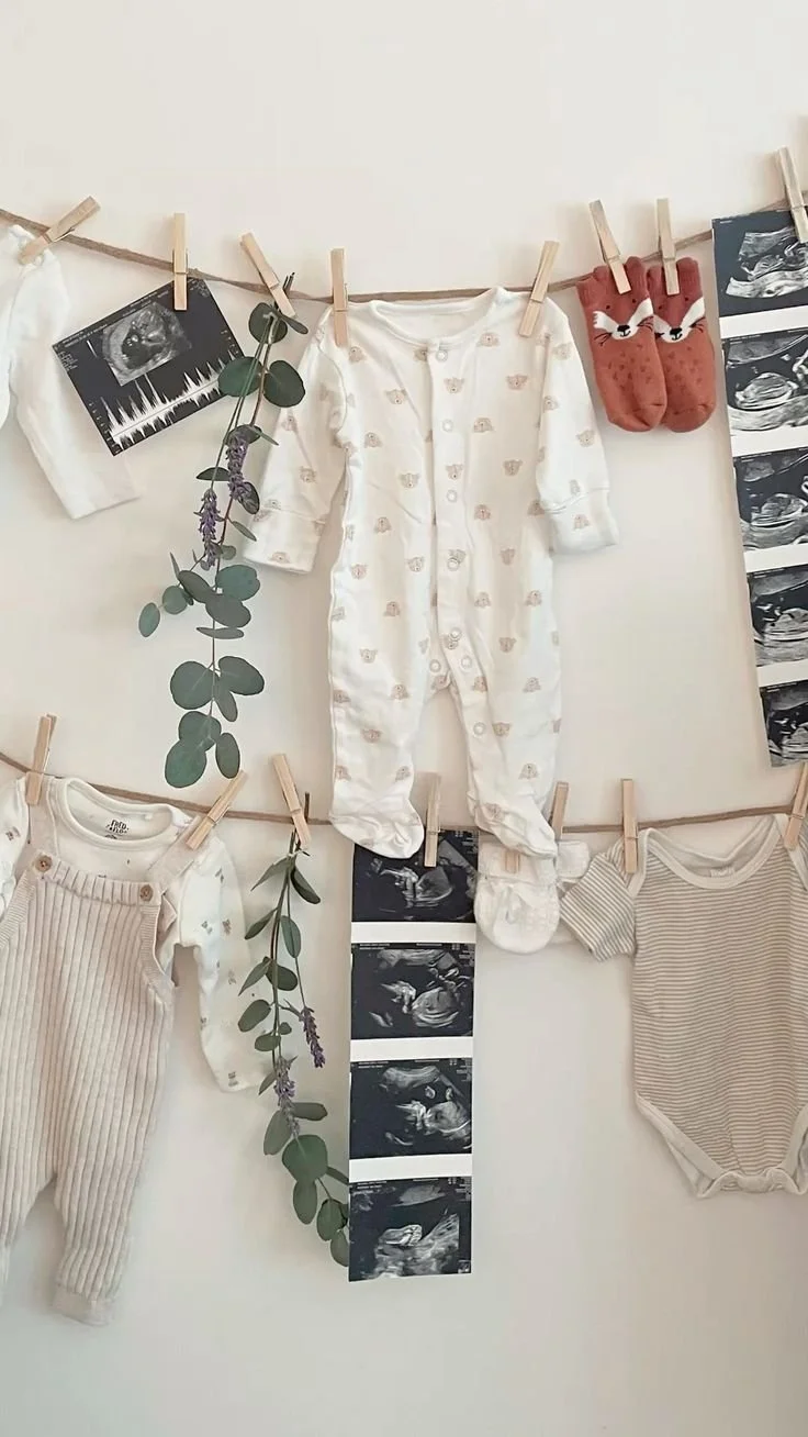 Baby clothes, ultrasound photos, and a sprig of eucalyptus hanging on a clothesline.