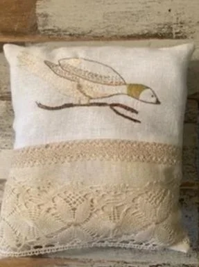 Decorative pillow with embroidery of a bird perched on a branch and lace details.