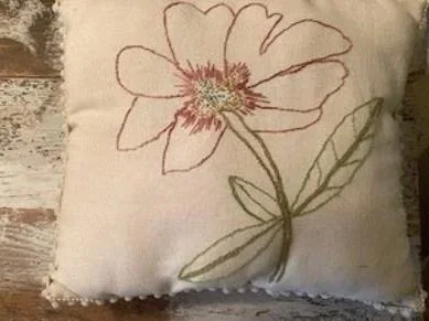 Decorative pillow with embroidery of a flower and leaf design.