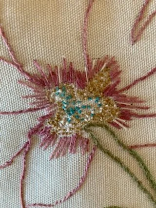 Close-up of embroidered flower with pink, green, and gold threads.