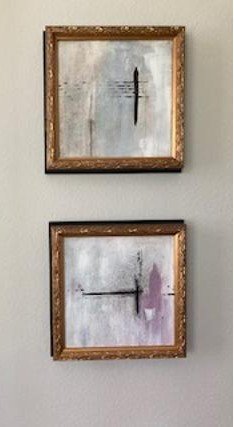 Two abstract paintings with wooden frames hanging on a wall, featuring minimalist lines and muted colors.
