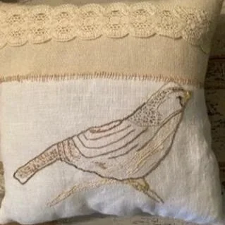 Decorative pillow with embroidered bird design and lace trim.