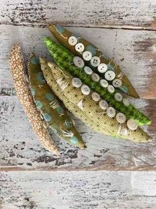 Five decorative fish-shaped objects made of fabric and buttons on a wooden surface.