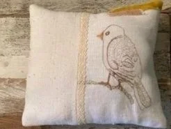 Decorative pillow with bird embroidery and lace, with a lemon slice on top.