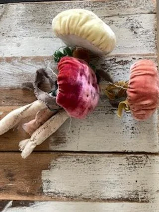 Three decorative faux pumpkins in yellow, pink, and orange with leaves and stems, arranged on a wooden surface.