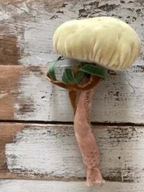 A mushroom with a yellow cap, a green soda can used as a base, and a small pink piece hanging below, built against a weathered wooden background.