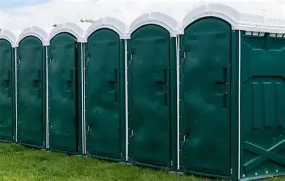 A row of six green portable toilets on grass, outdoors.