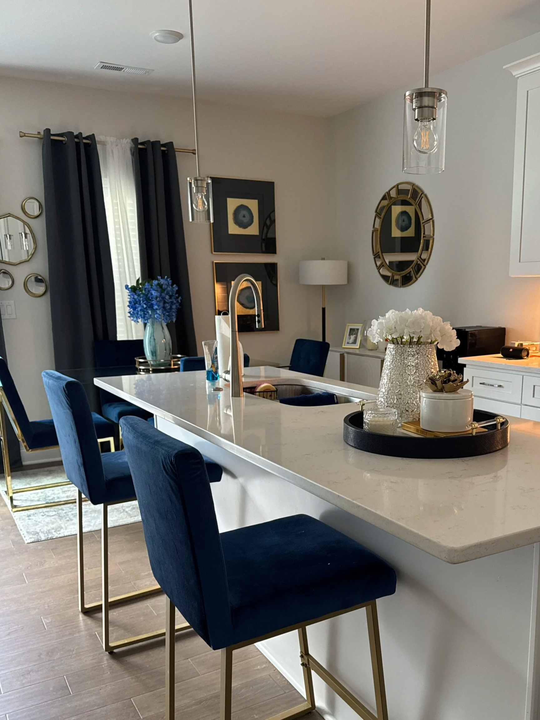 Modern kitchen and dining area with a white marble island, navy blue chairs, and gold accents. Decor includes blue flowers, white flowers, mirrors, and framed artwork in Oak Ridge home.
