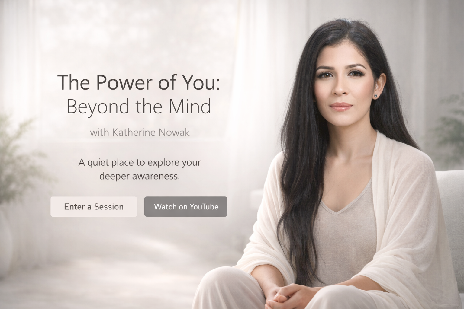 A woman with long dark hair sitting on a light-colored sofa in a bright, softly-lit room, looking directly at the camera with a neutral expression.