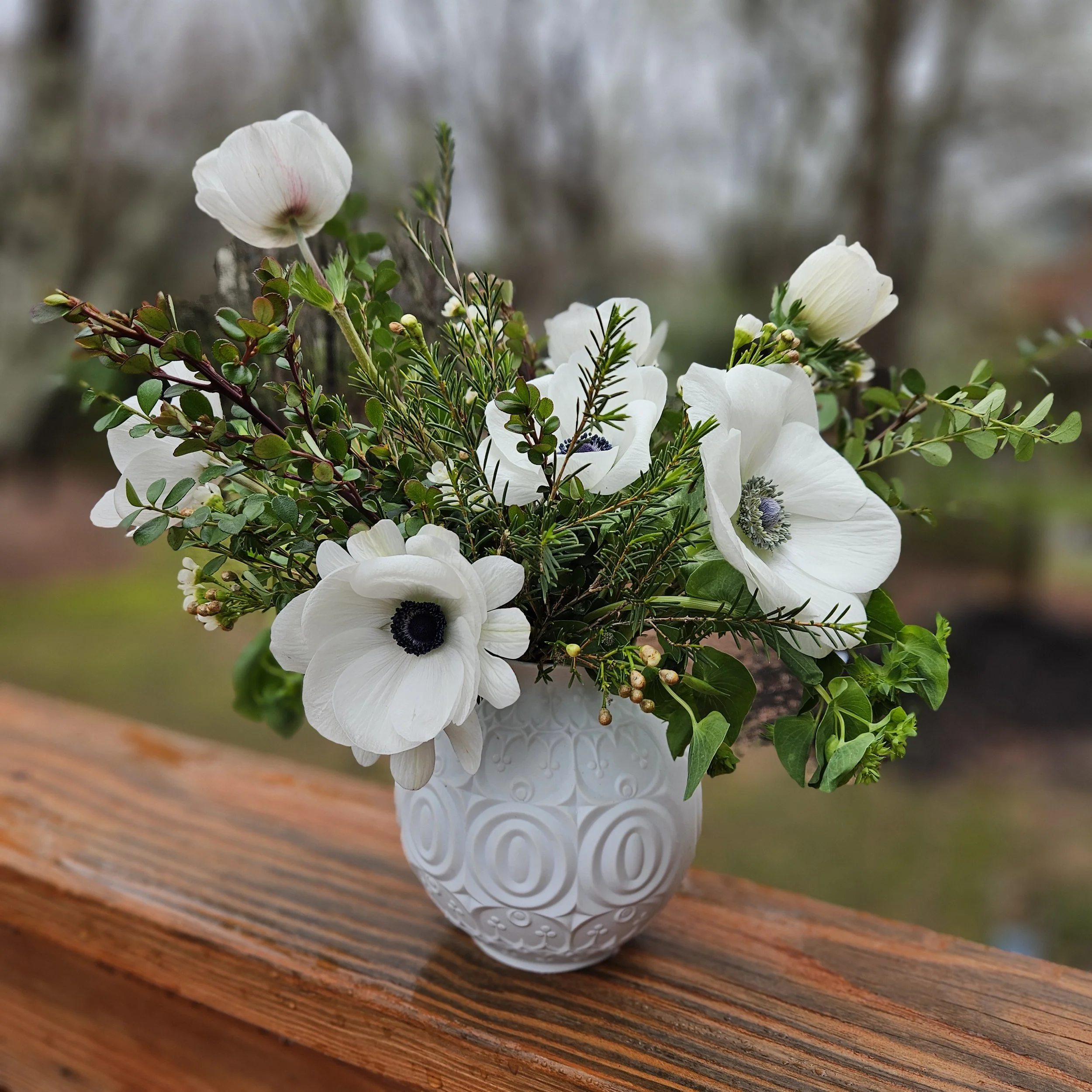 Fresh flower arrangement of elegant white anemones and spring green foliage in a vintage white vase