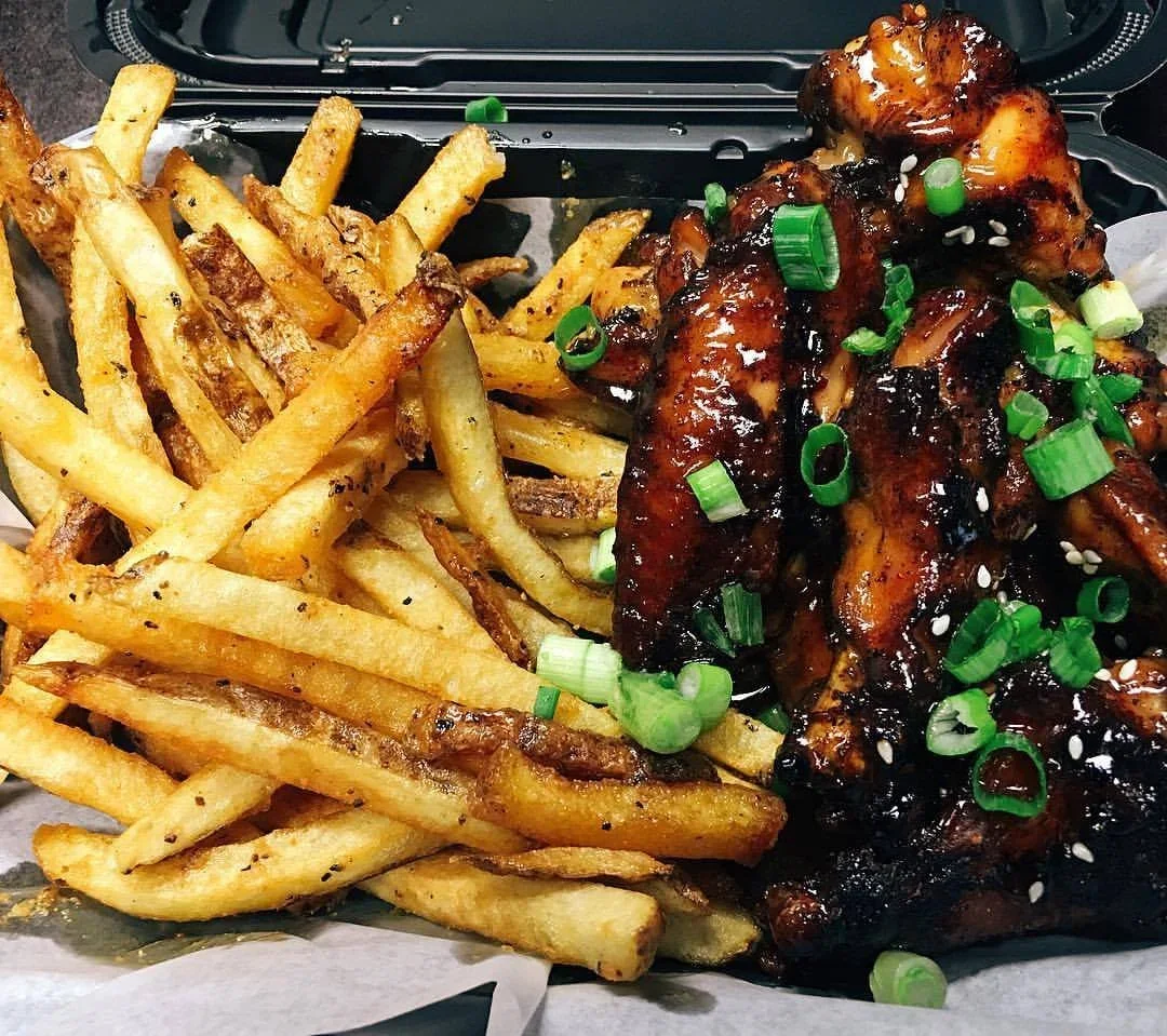 French fries and chicken wings topped with green onions and sesame seeds, served in a takeout container.