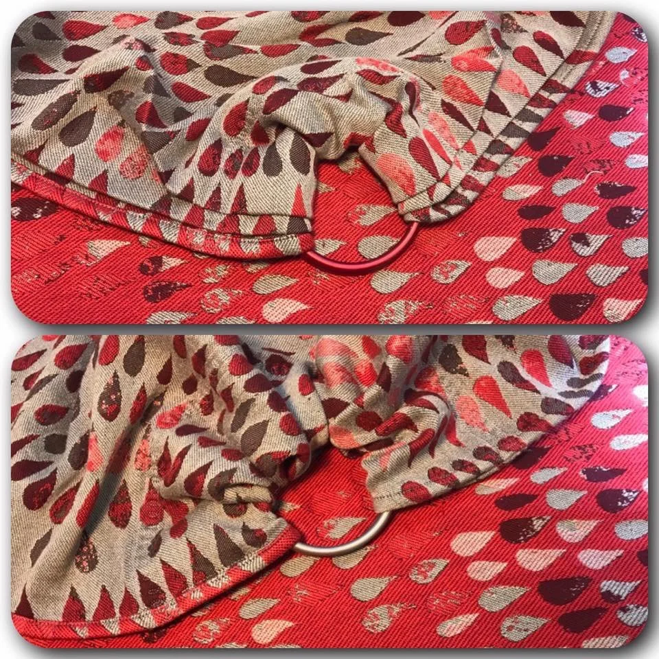 Close-up of a beige scarf with red and black leaf patterns, draped over a red fabric with a heart pattern, secured with a red metal ring.