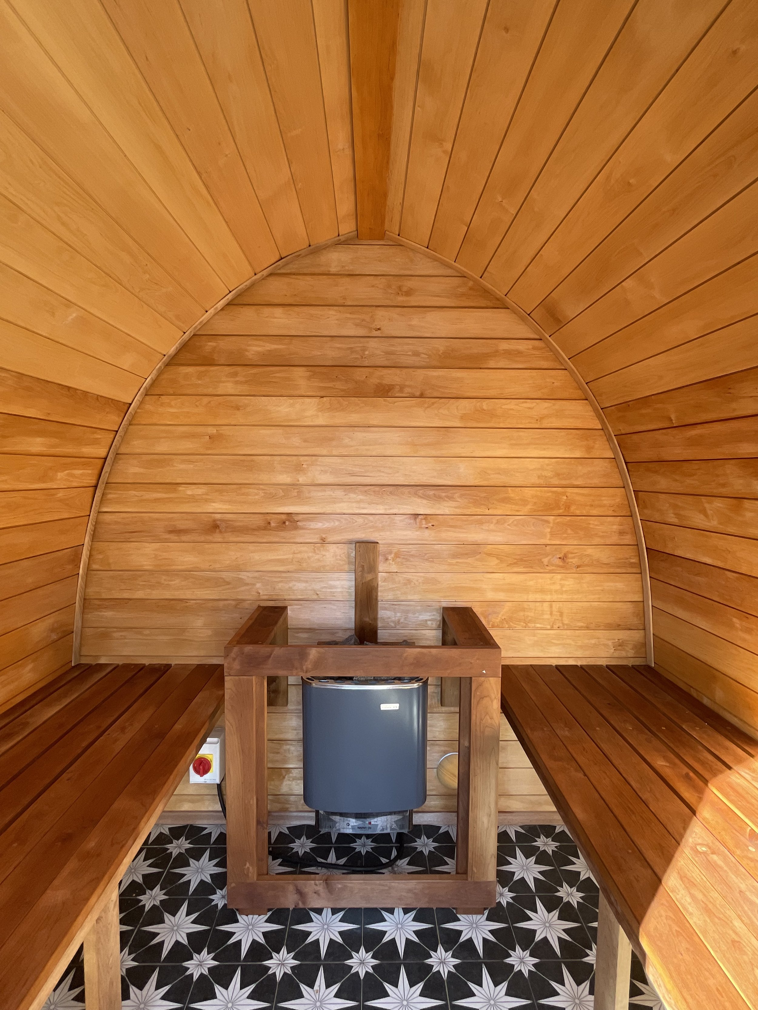 Interior of a small, rounded sauna with wooden walls, benches on each side, and a heater in the center.