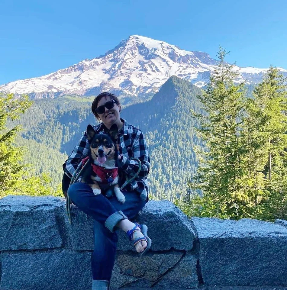 young woman holding a corgi and sitting in front a view of Mt. Rainier