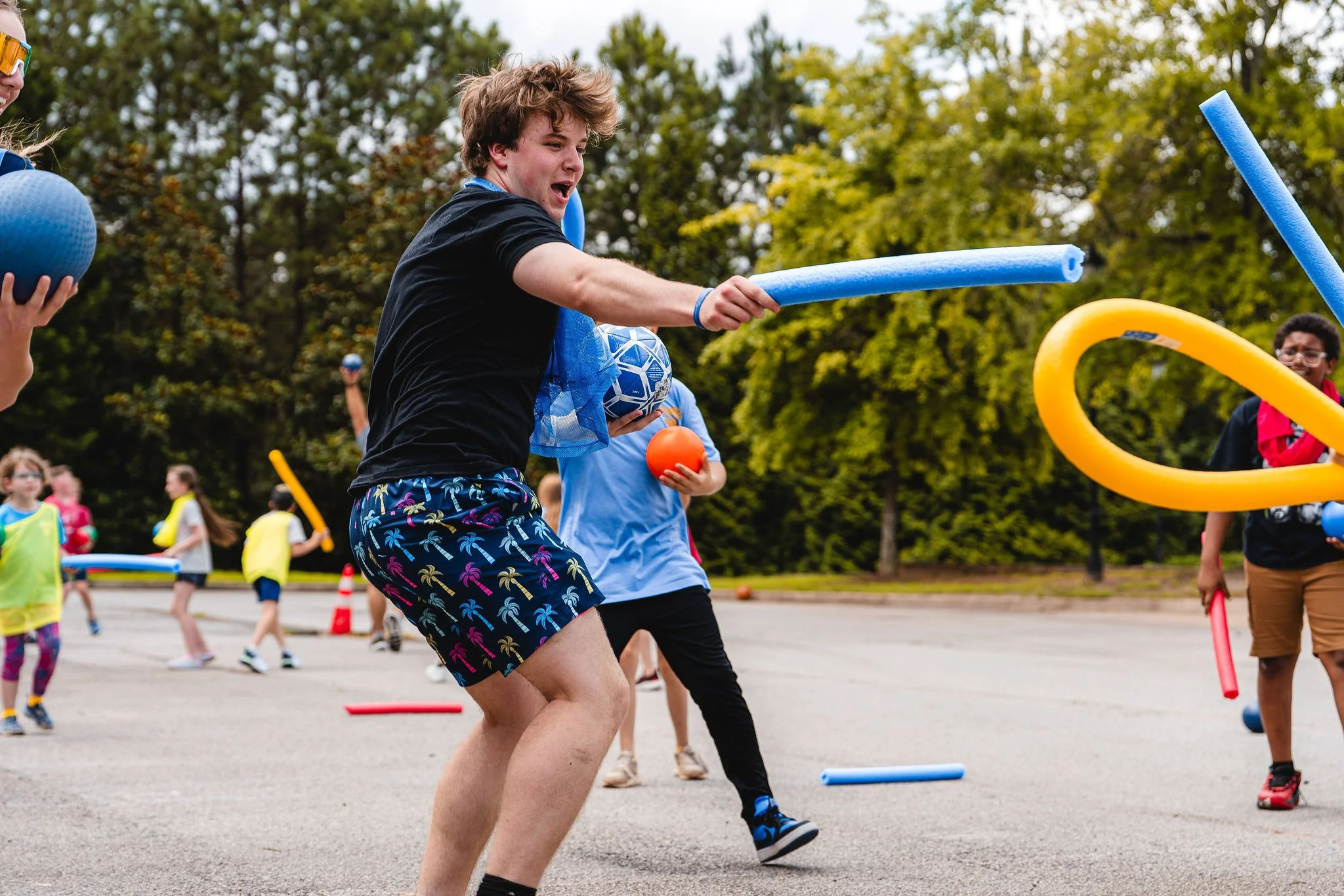 Children playing outdoors with foam pool noodles and balls during a fun activity or game.