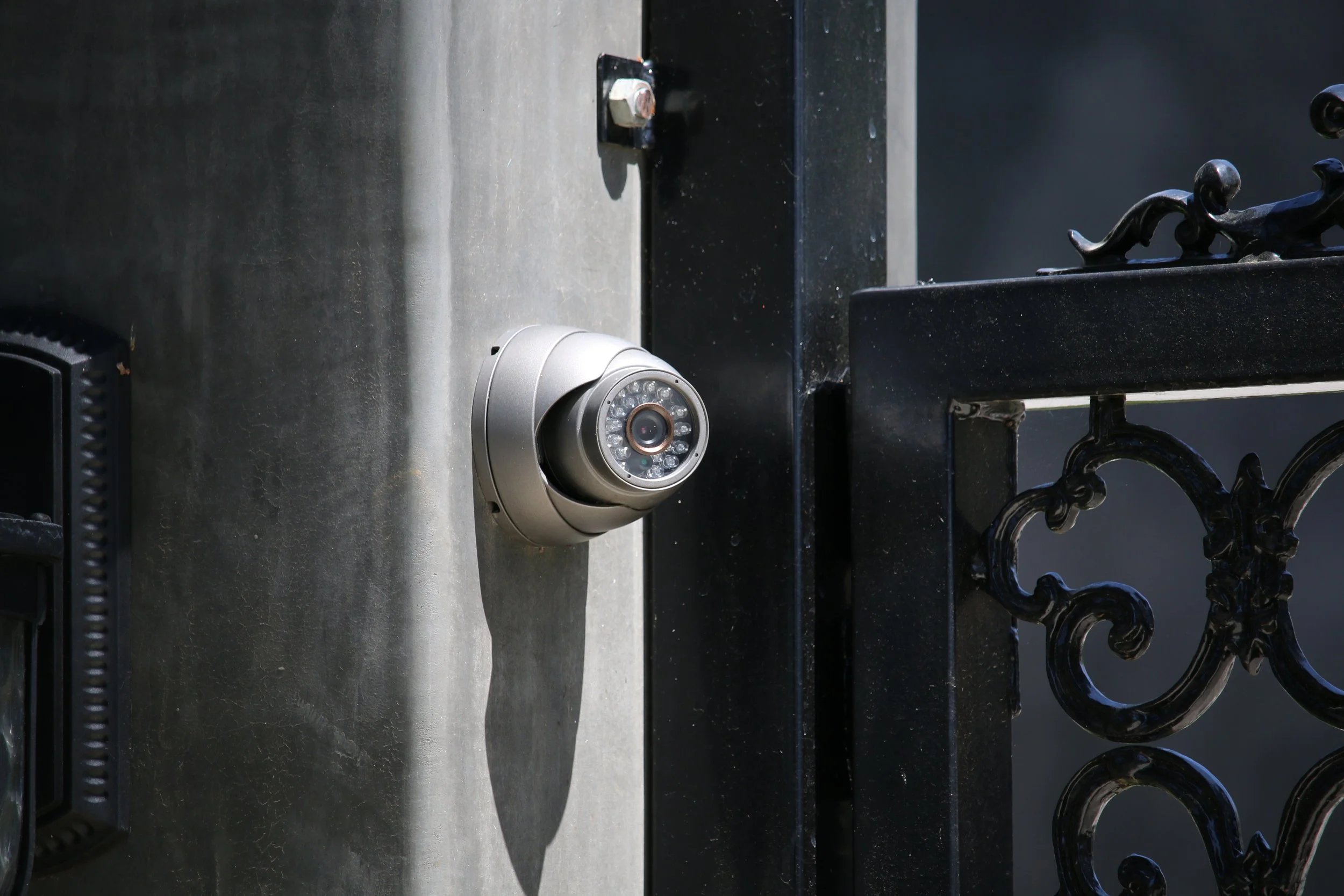 A security camera mounted on a concrete wall next to a black metal gate.