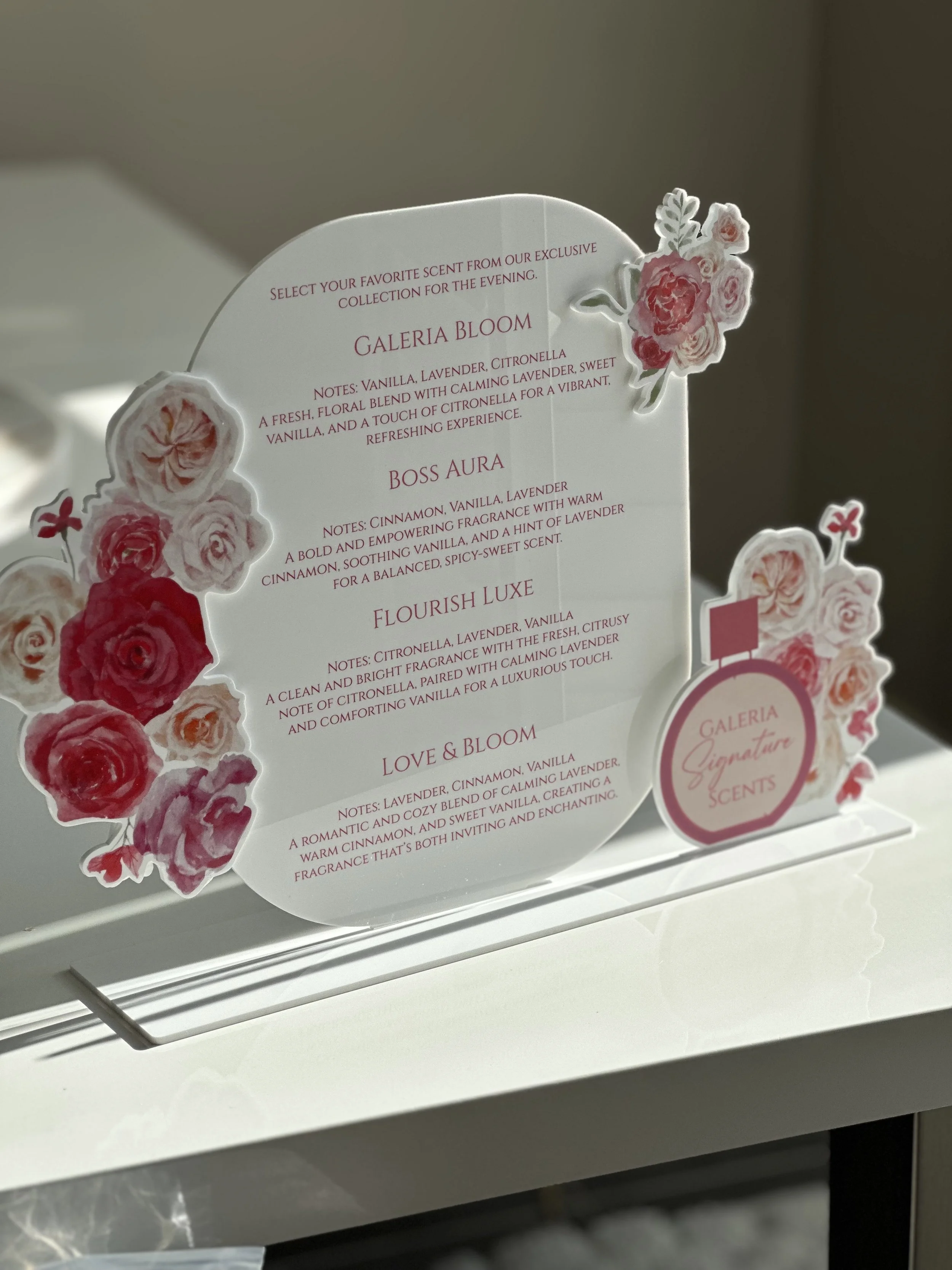 Sign with descriptions of floral scents including Galeria Bloom, Boss Aura, Flourish Luxe, and Love & Bloom, decorated with pink and red floral illustrations.