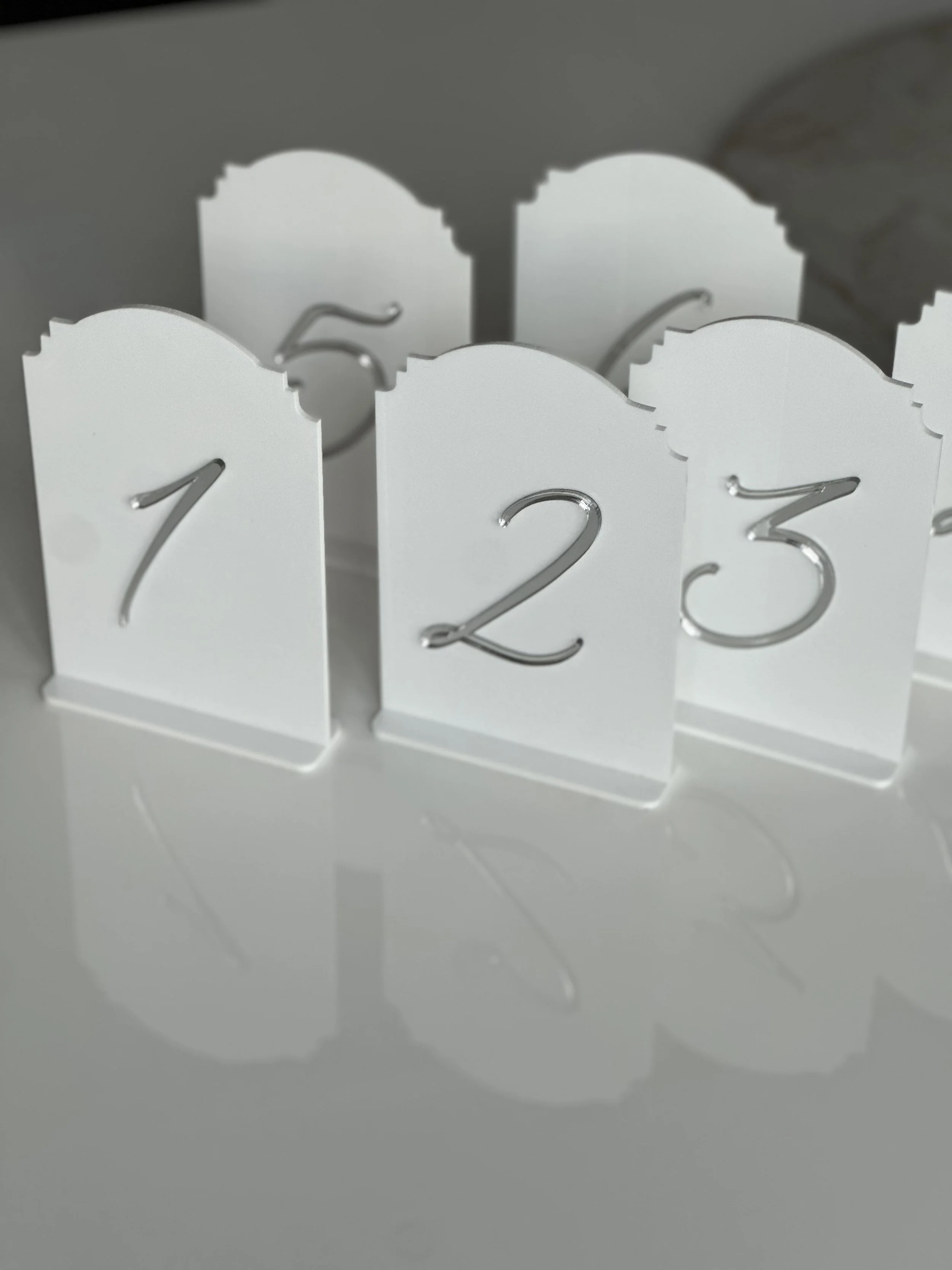 White decorative calendar displaying the numbers 1, 2, and 3, with silver numbers and scalloped edges, reflecting on a glossy white surface.