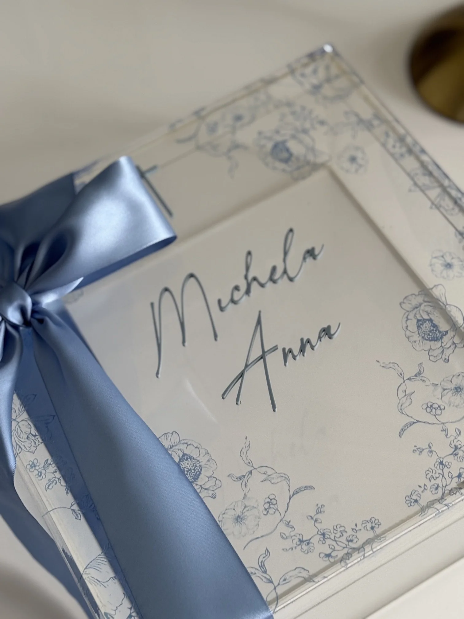 A card with floral designs and handwritten text, decorated with a blue ribbon on the corner.