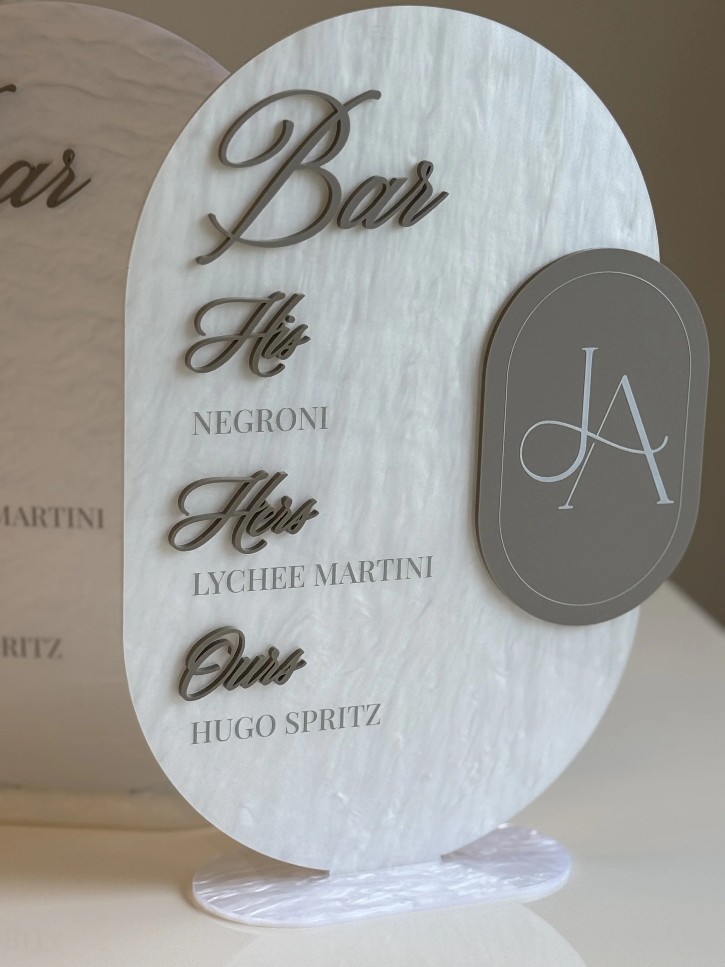 A circular sign with a white background and black text that reads 'Bar His' and 'Negroni Lychee Martini' and a gray oval sign with white initials 'LA'.