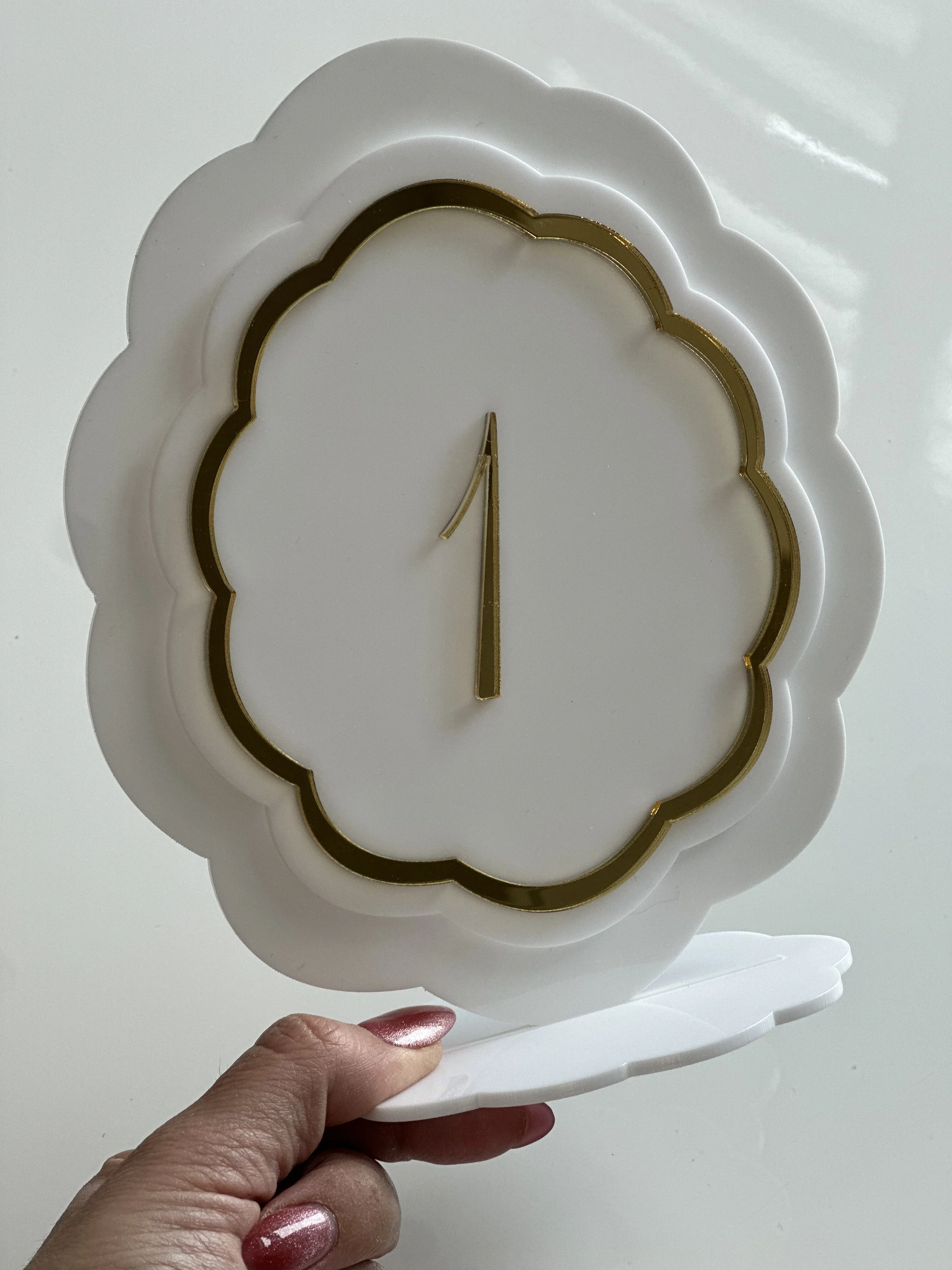 White decorative clock with gold accents, held by a person with painted nails.