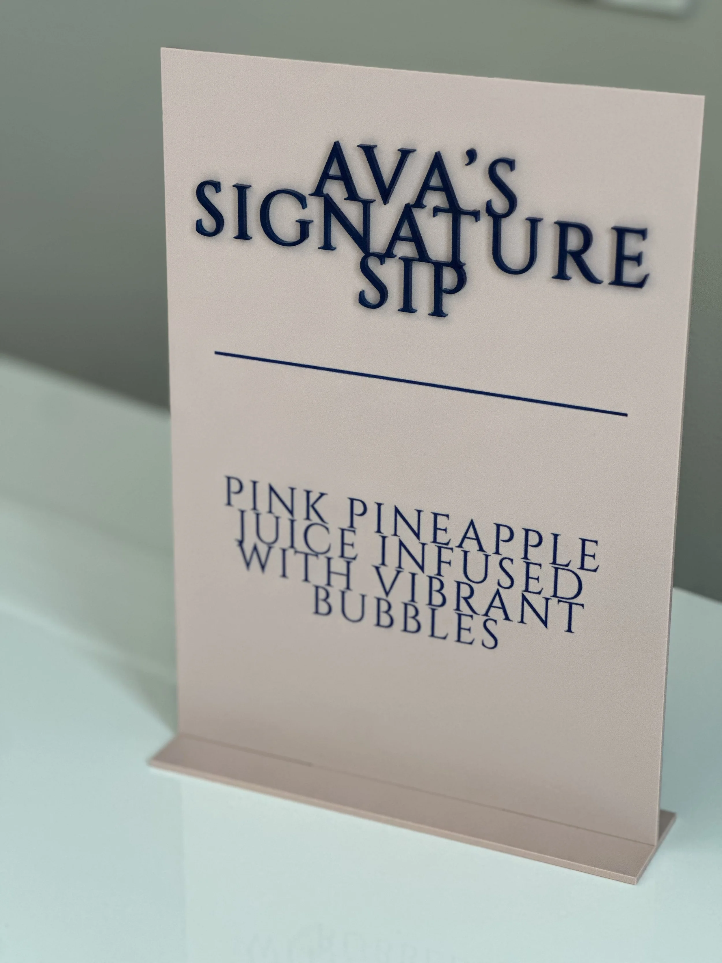 Sign with party punch details, labeled 'Ava's Signature Sip', describing pink pineapple juice infused with vibrant bubbles.