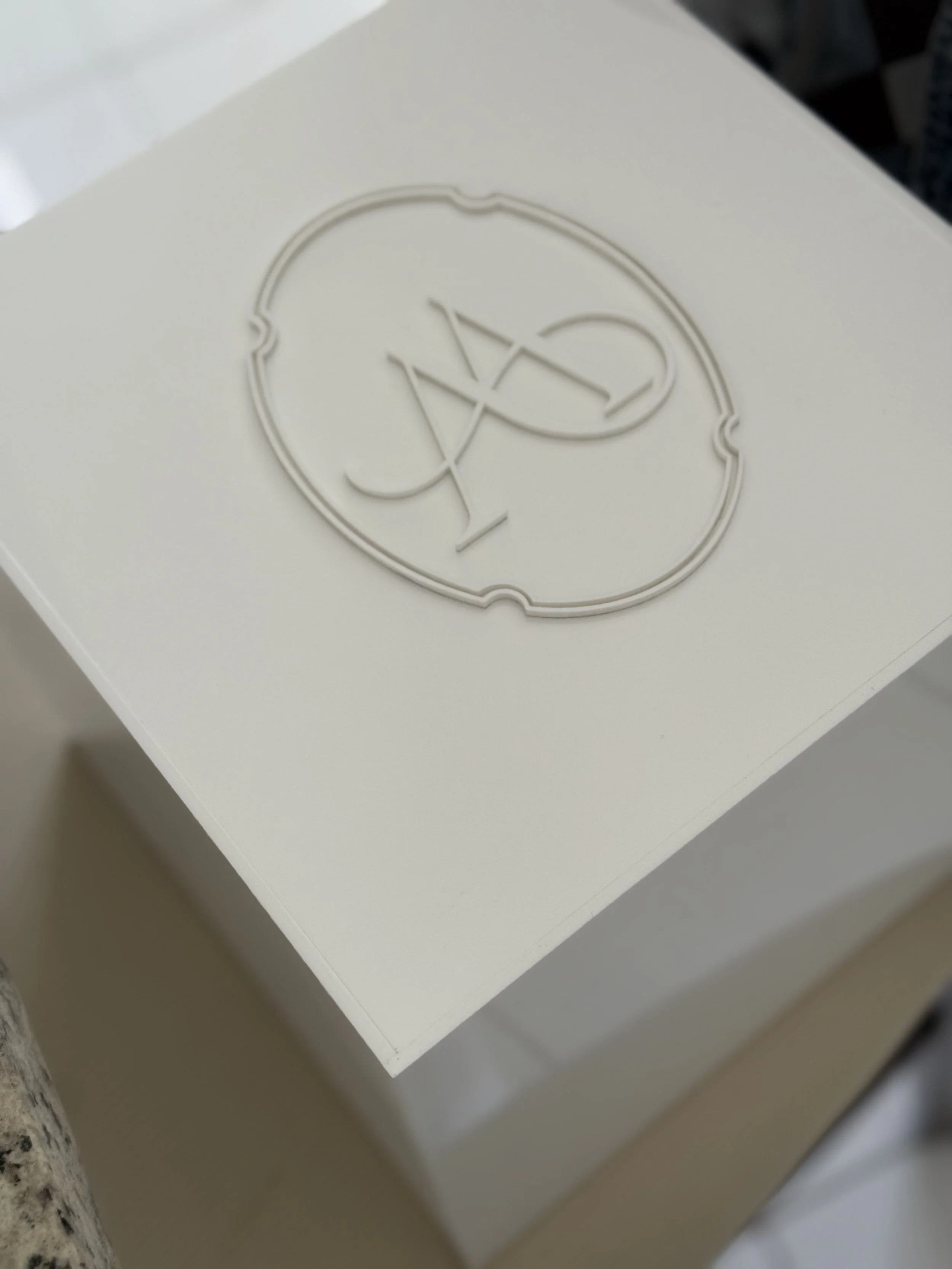A white box with a raised logo featuring a circular design and monogram letters.
