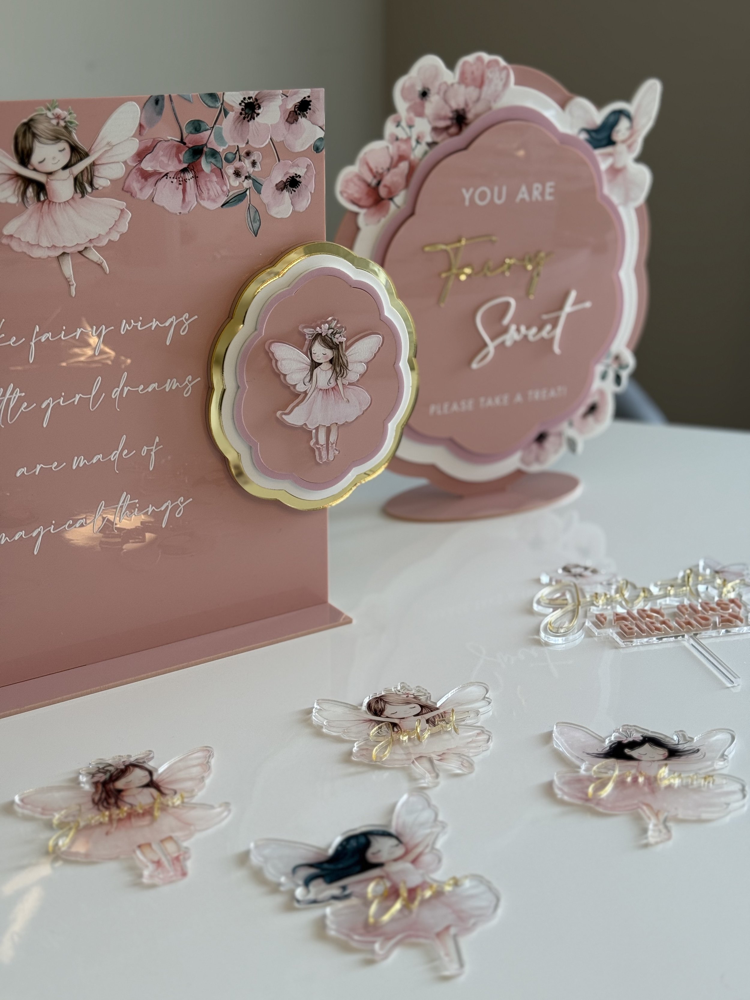 Pink fairy-themed decorations featuring illustrated fairy characters and floral accents, with signs saying "You are fairy sweet" and inspirational quotes.