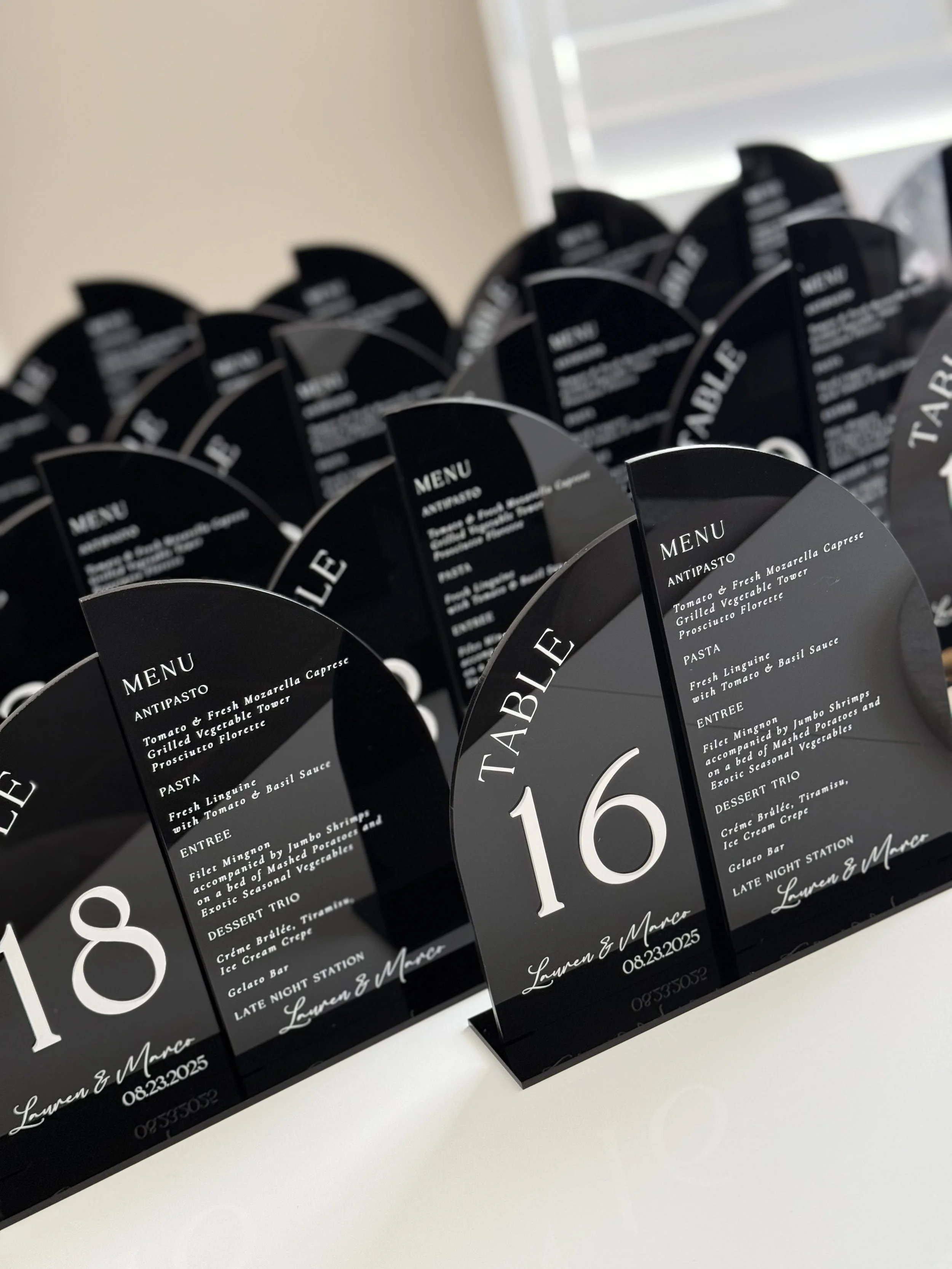 Black menu cards with white text displaying a wedding event, numbered 8 and 16, with guest names Lauren and Marc, and the date 08.23.2025.