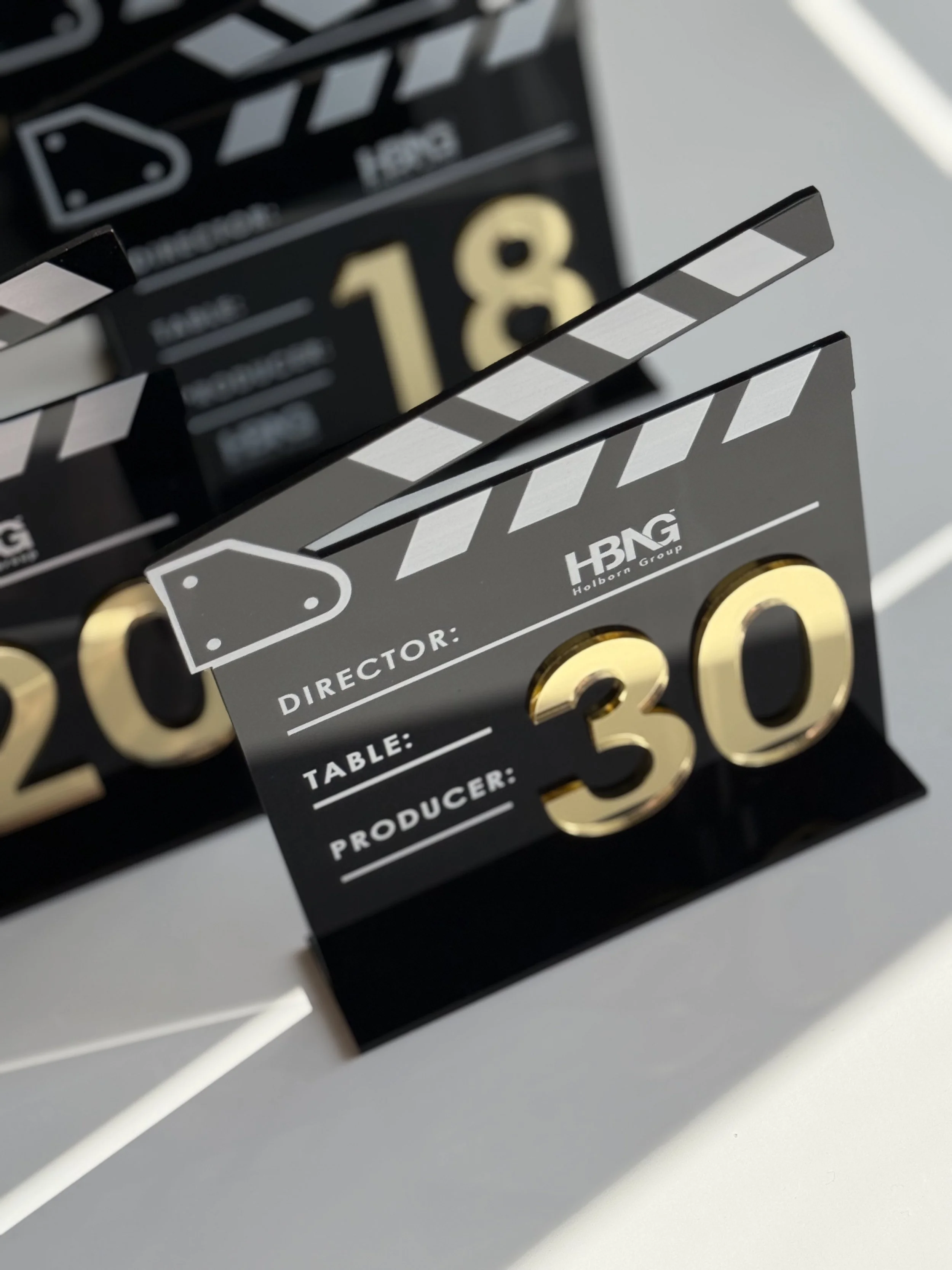 Clapperboard with black and gold accents displaying the number 30, used in film production, with fields for director, table, and producer, branded with Holborn Group logo.